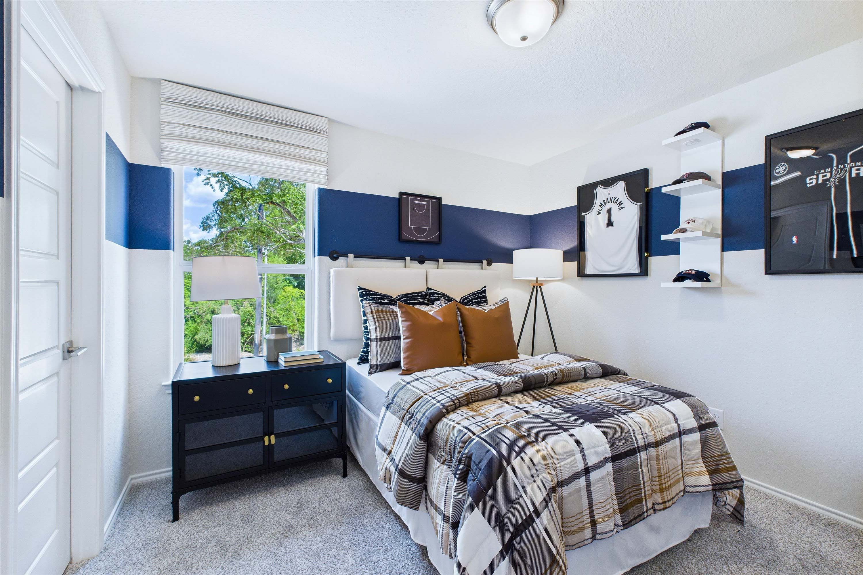 Spacious secondary bedroom in The Gillian C model home with San Antonio Spurs themed decor and plaid bedding.
