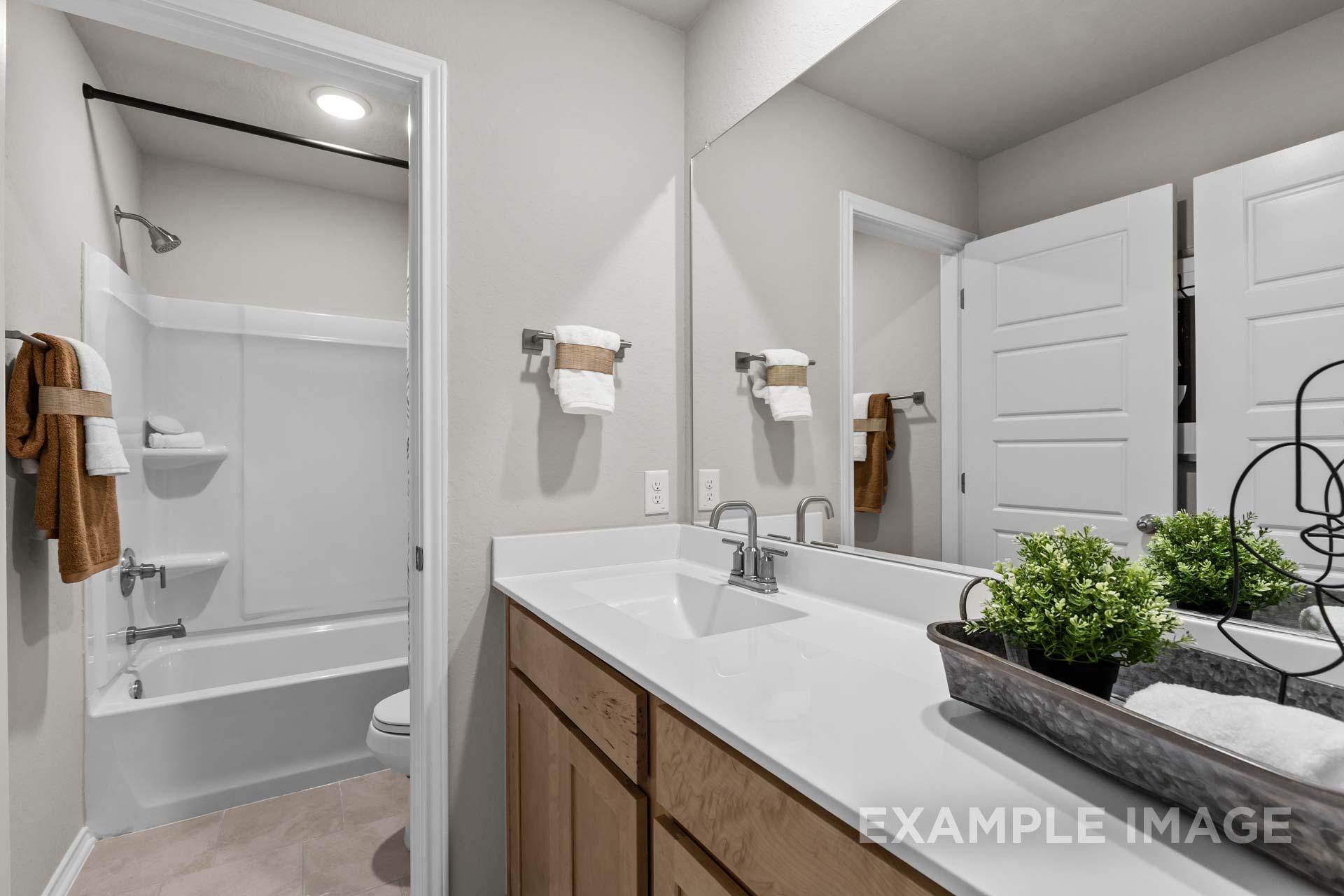 Modern guest bathroom featuring tub-shower combo, white quartz vanity, and wood cabinets in 5-bedroom Sabine J home, Heartland Texas