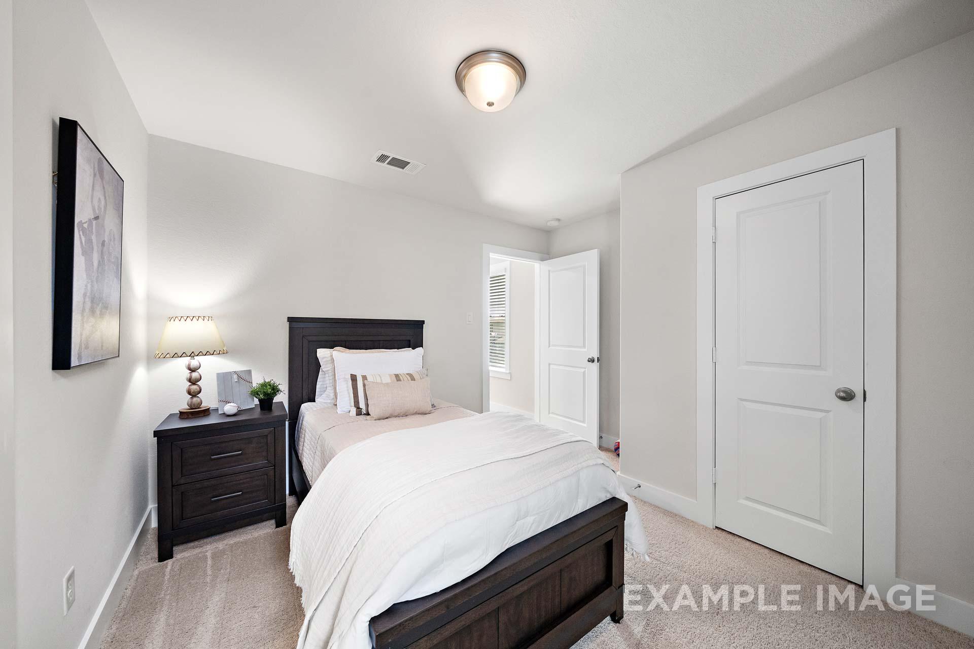 Cozy secondary bedroom in The Lily A Davidson Homes design with wooden bed, neutral gray walls, abstract art