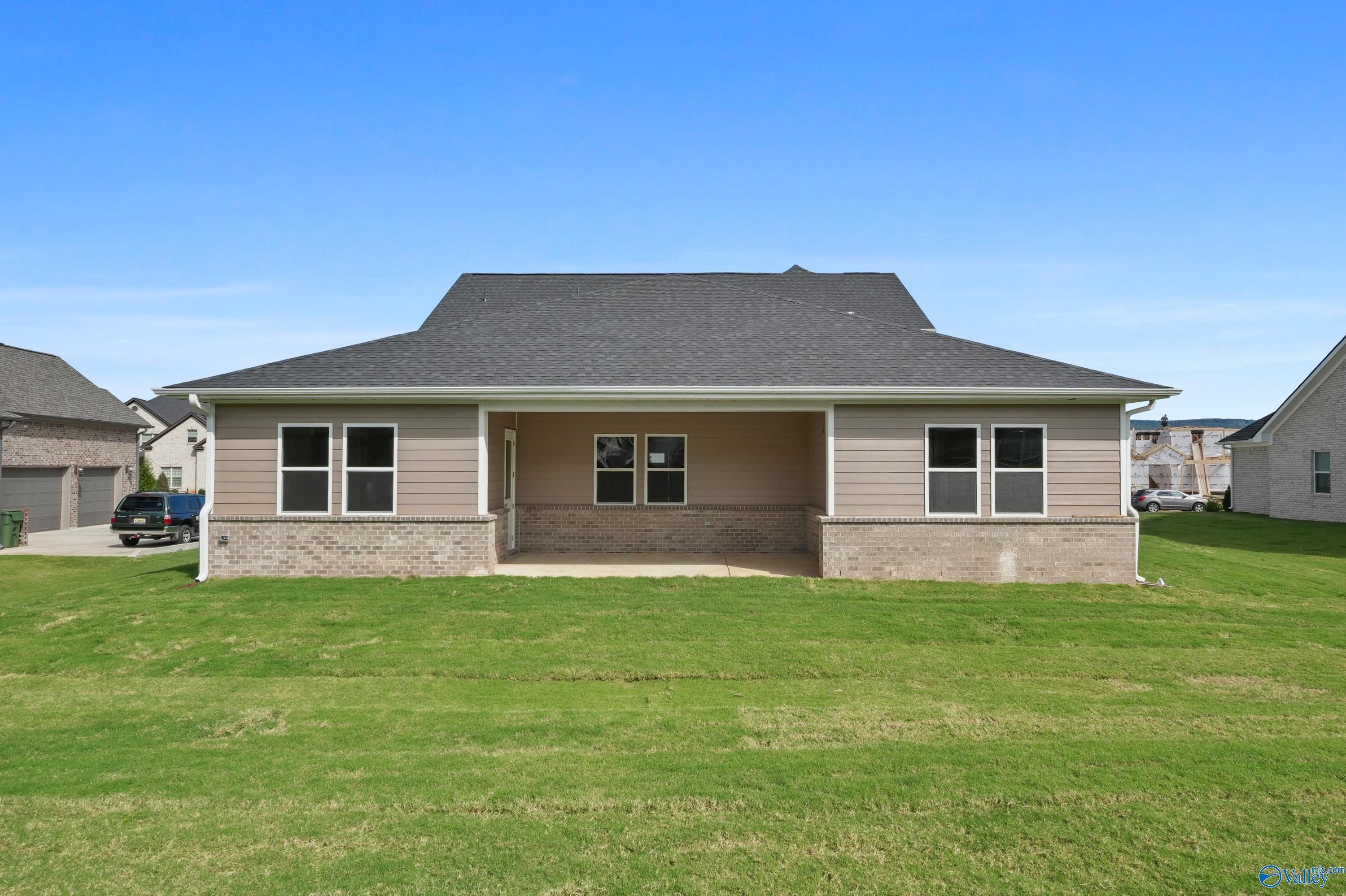 Two-story beige home exterior with 3-car garage, covered porch, brick accents, and green lawn in Owens Cross Roads, Alabama