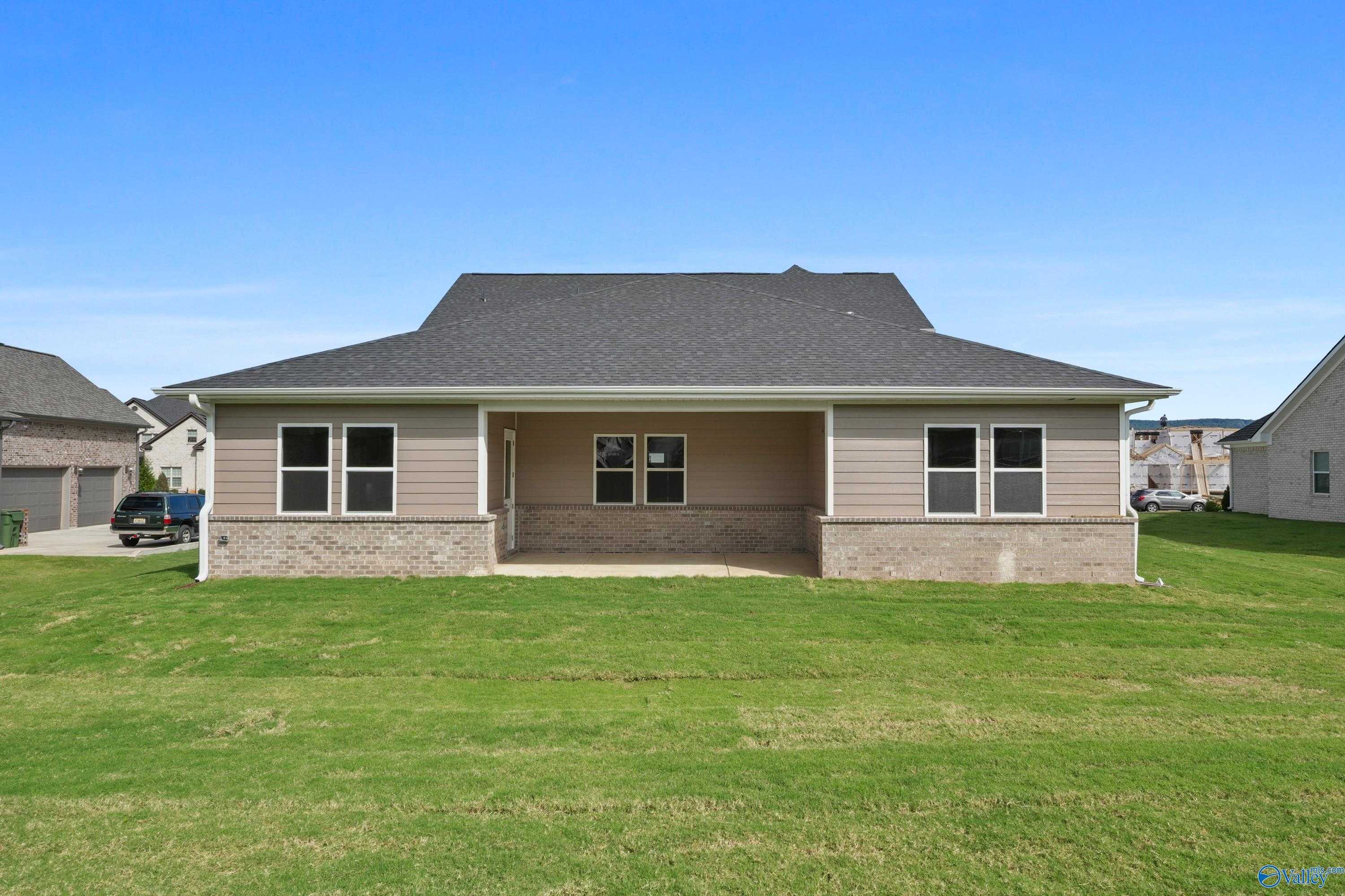 Two-story beige home exterior with 3-car garage, covered porch, brick accents, and green lawn in Owens Cross Roads, Alabama