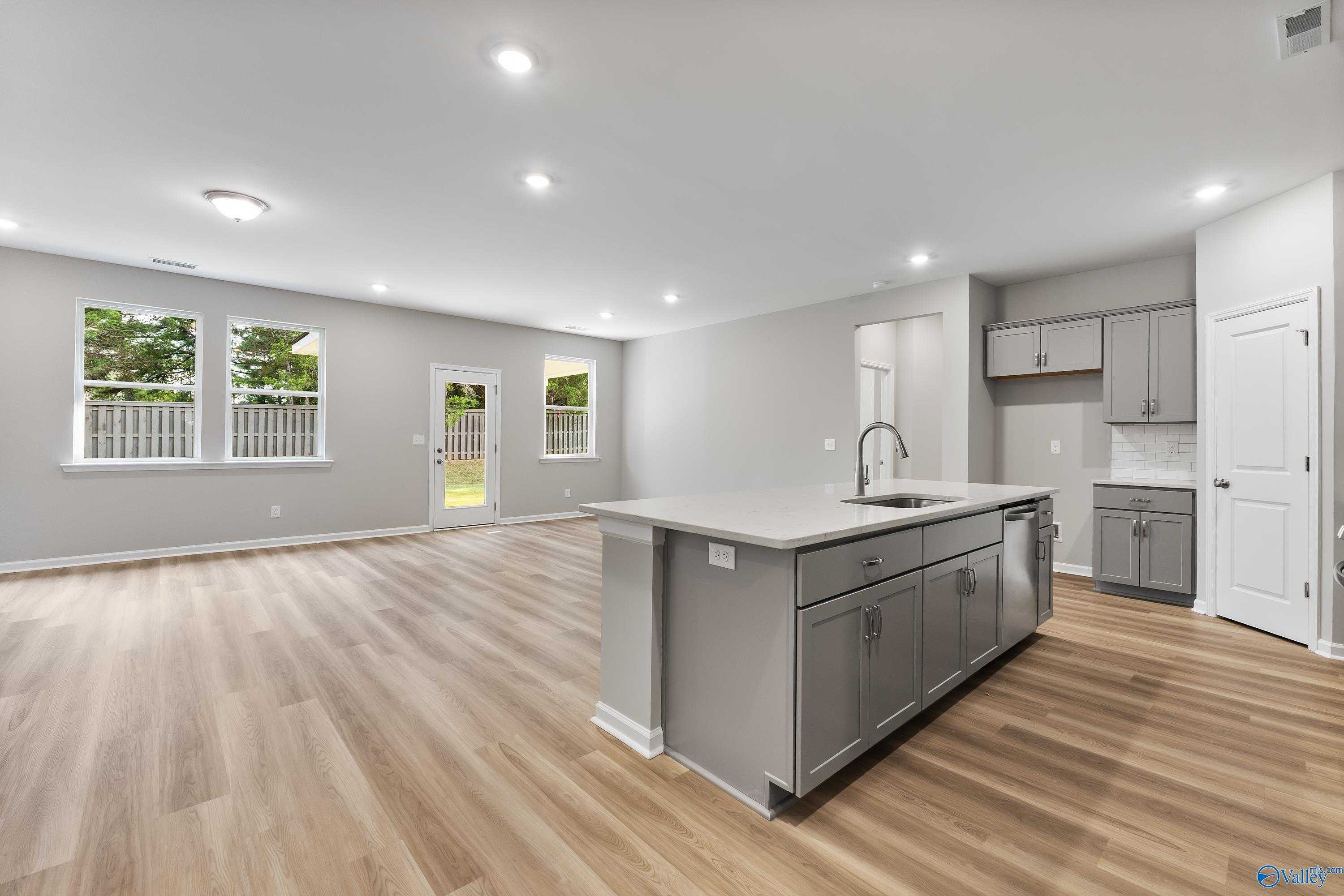 Open-concept kitchen with gray shaker cabinets, white quartz island, and backyard views in The Grace 3-bedroom home, Evergreen Mill, Madison, Alabama