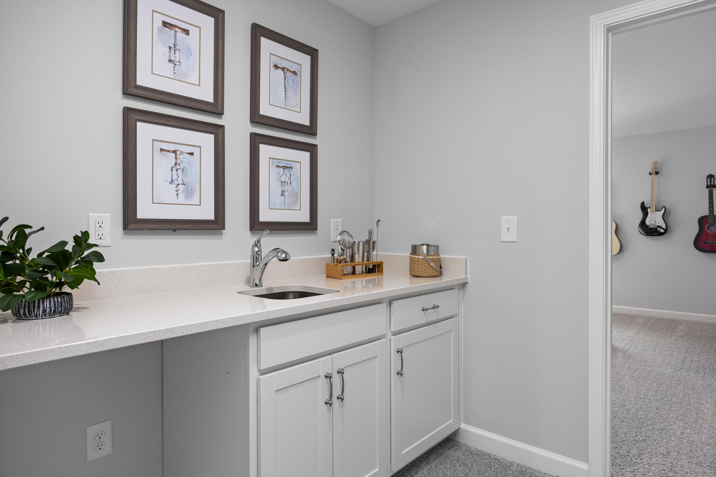 Spacious utility sink area in The Magnolia A home with white quartz countertop, cabinetry, framed art, potted plant, and hanging guitars