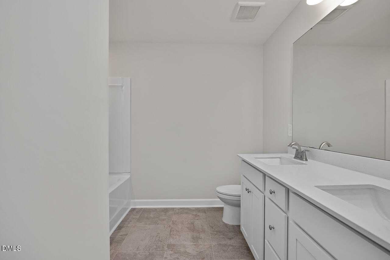 Modern double-sink vanity bathroom with soaking tub and large mirror in Davidson Homes The Warren floor plan, Fuquay-Varina, NC
