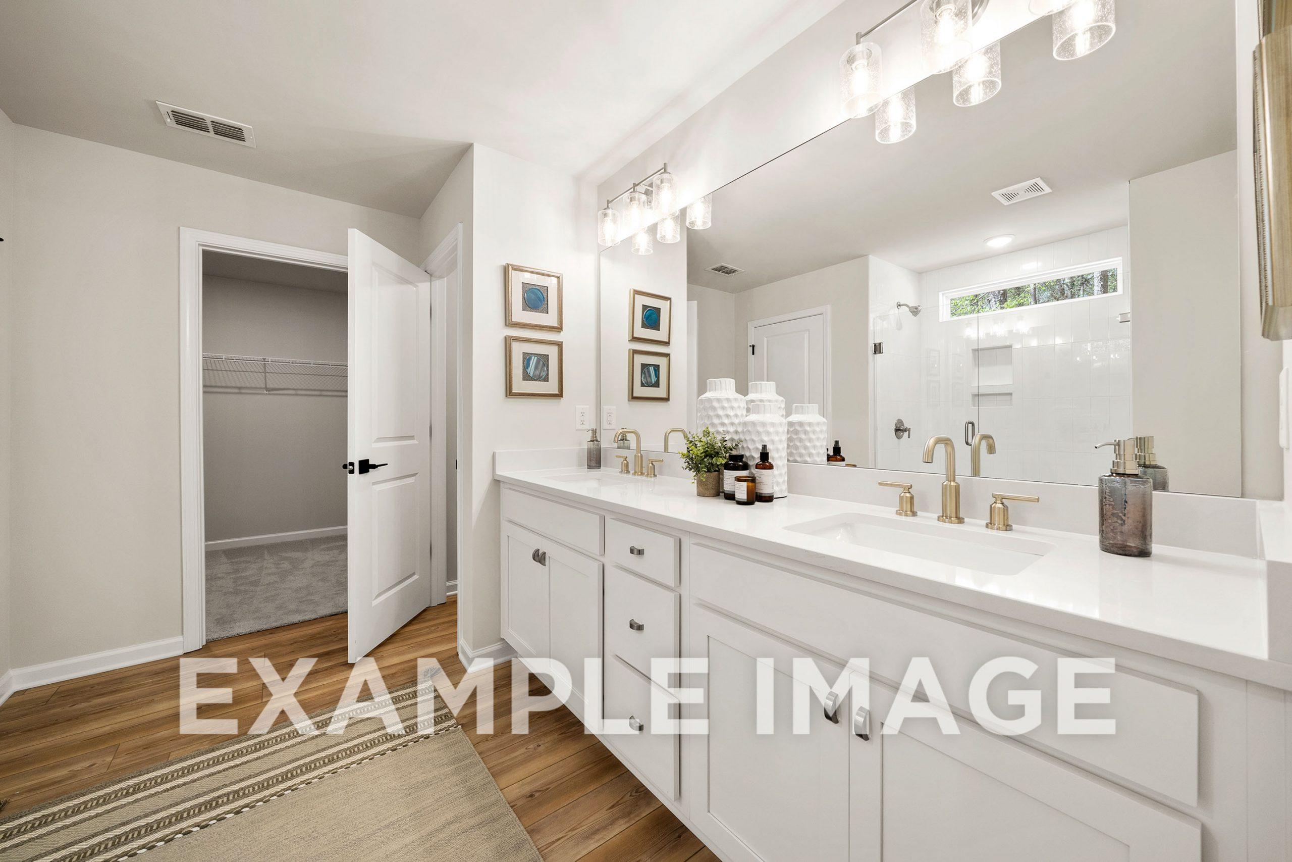 Luxurious master bathroom in The Hickory B featuring white double vanity, large mirror, walk-in closet, and glass shower