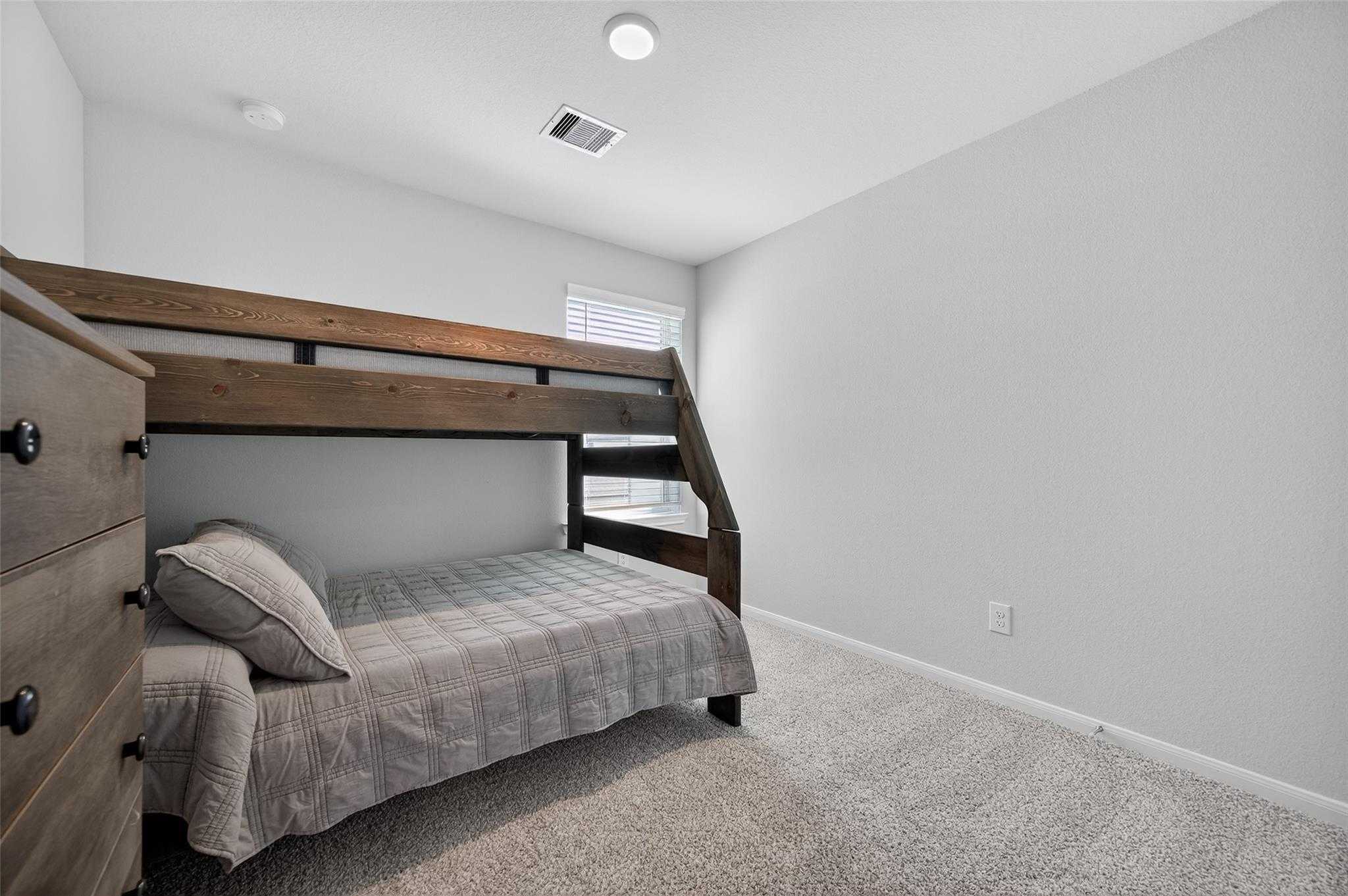 Wooden bunk bed with gray bedding in light gray upstairs bedroom, The Brazos E by Davidson Homes, Magnolia, Texas