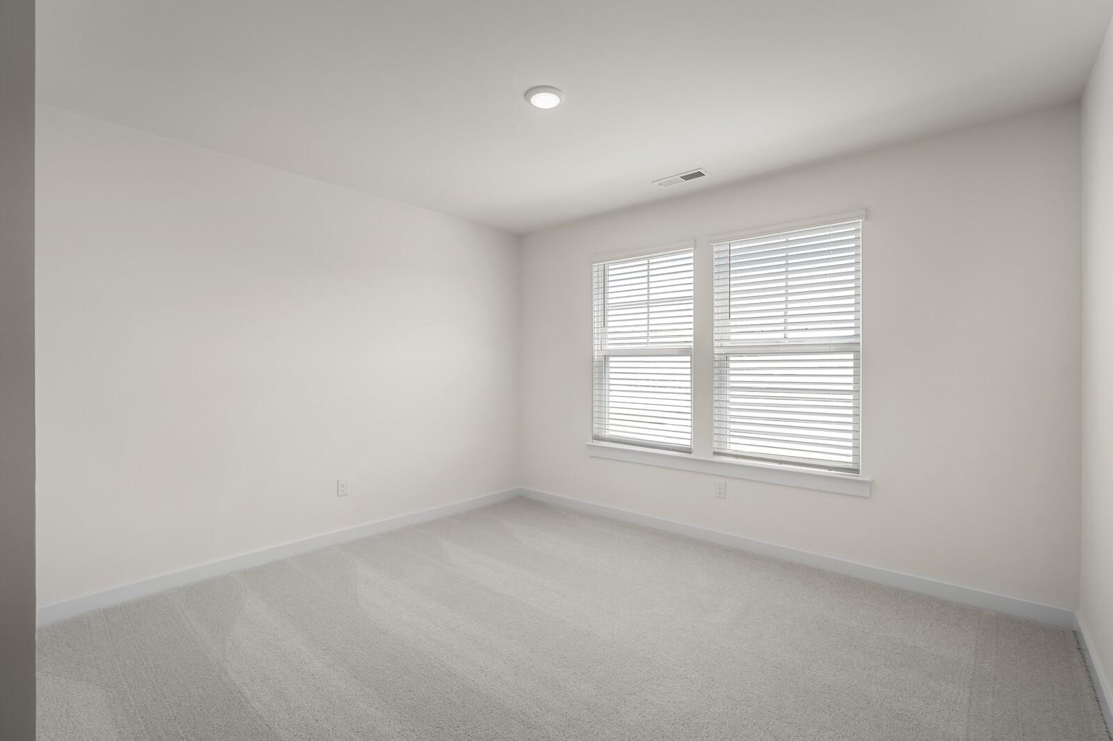 Bright, carpeted bedroom with neutral walls and windows in The Willow floor plan at Woods Crossing, Gallatin, Tennessee.