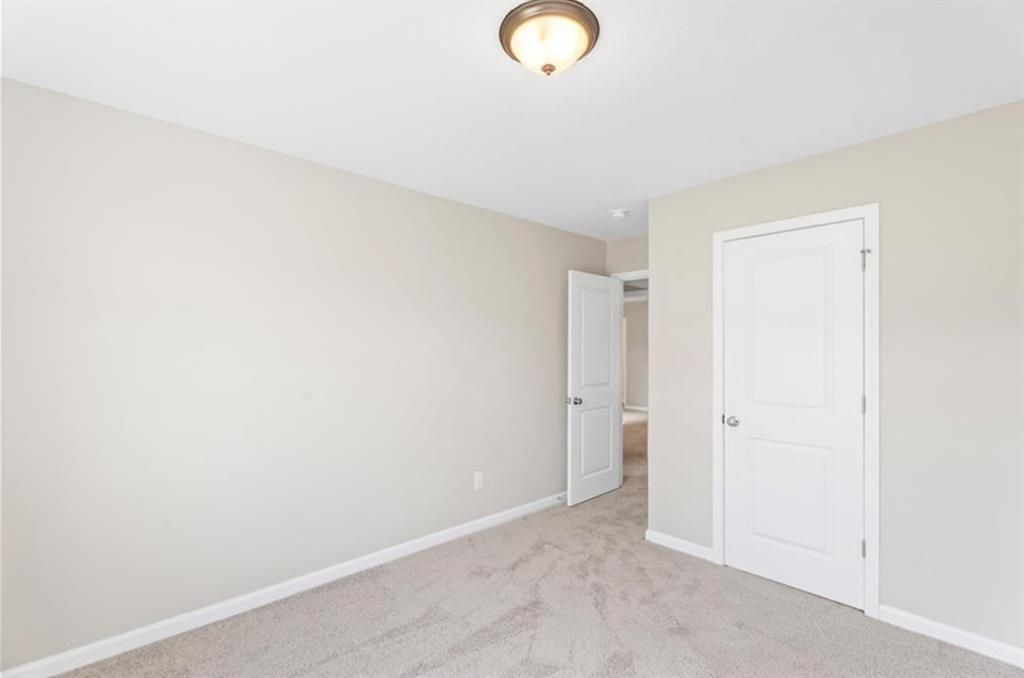 Cozy secondary bedroom with beige walls, plush carpet, and open bathroom door in Davidson Homes The Washington, Phenix City, Alabama