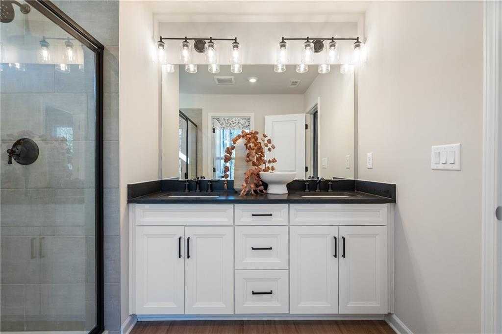 Elegant master bathroom double vanity with white shaker cabinets, black hardware, and glass shower in Davidson Homes The Marion C, Winder, Georgia