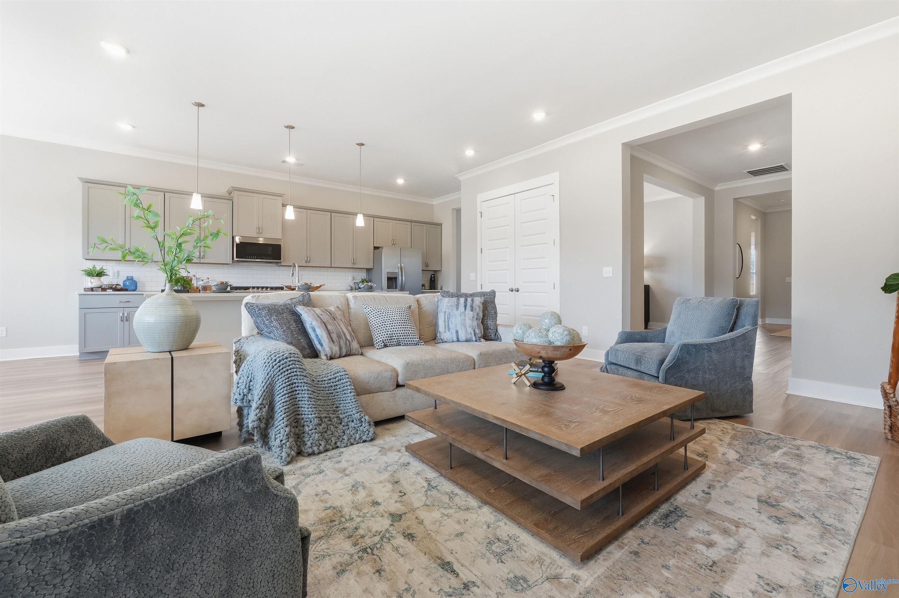 Open-concept living room with gray sectional sofa, wood coffee table, and adjacent kitchen with stainless appliances in Evermore Homes The Oxford B, Owens Cross Roads, AL