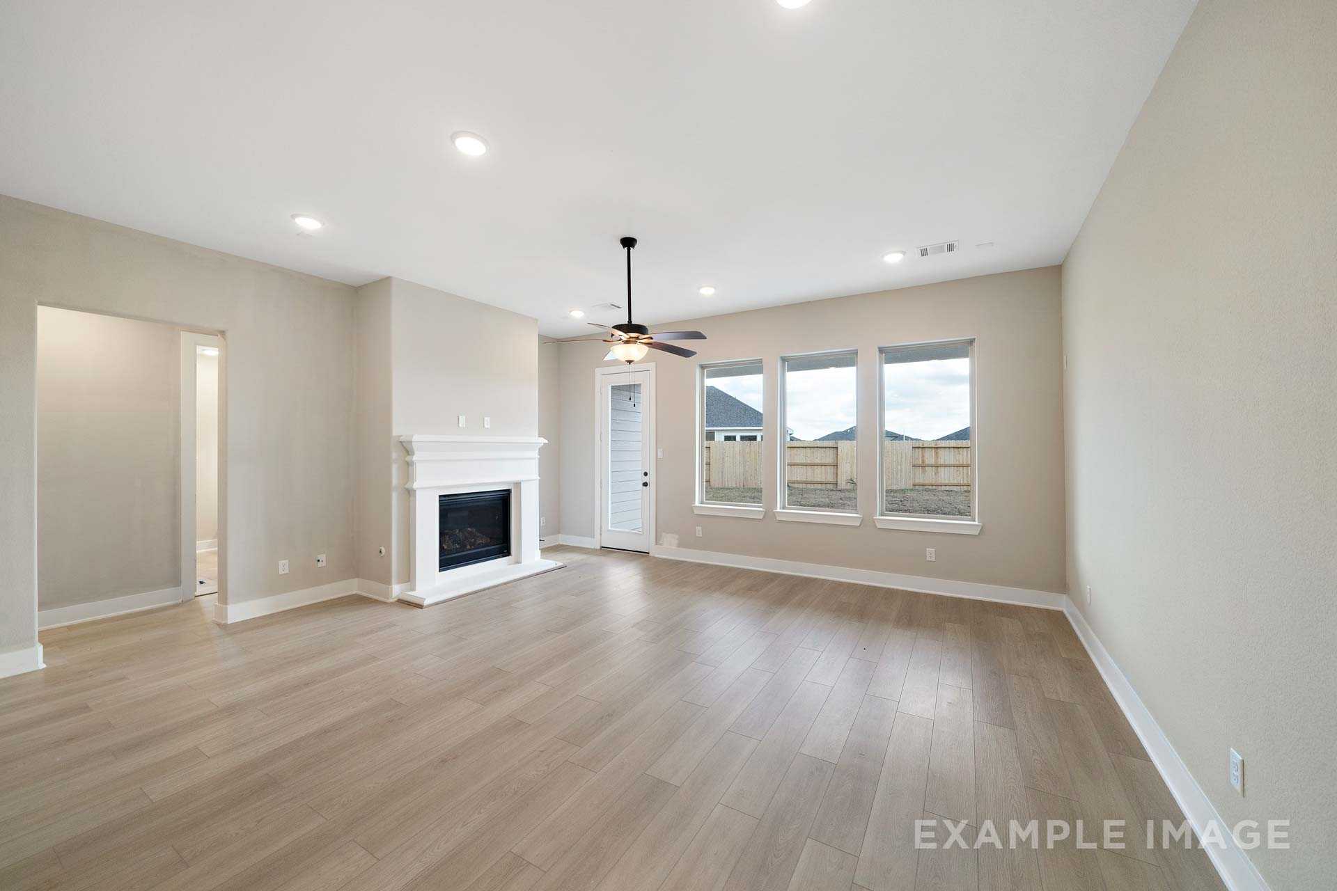 Spacious living room in The Elizabeth A home design with stone fireplace, ceiling fan, large windows, and light wood floors