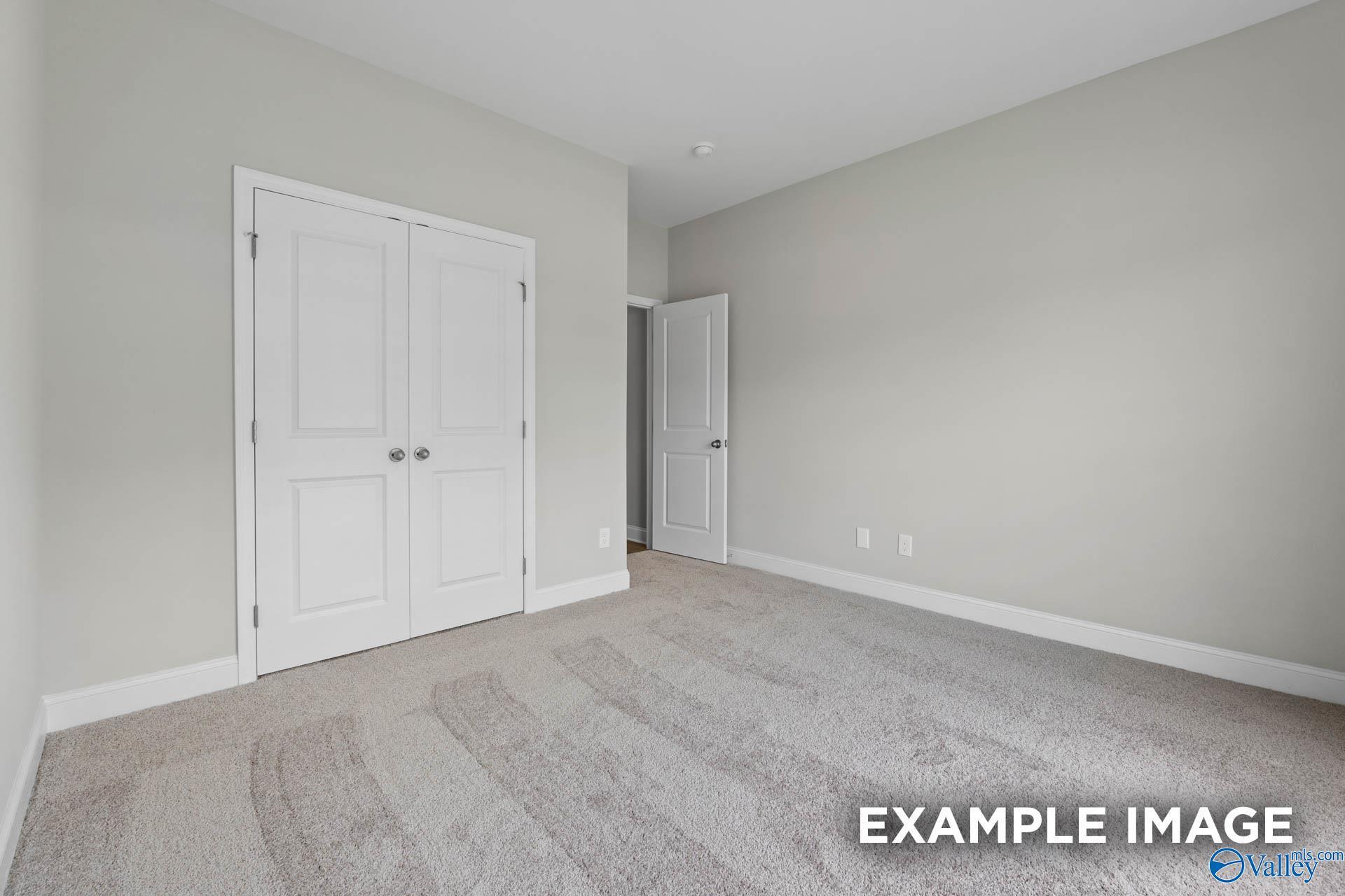 Spacious bedroom with double white closet doors, light gray walls, and beige carpet in Davidson Homes The Everett B, Athens, Alabama
