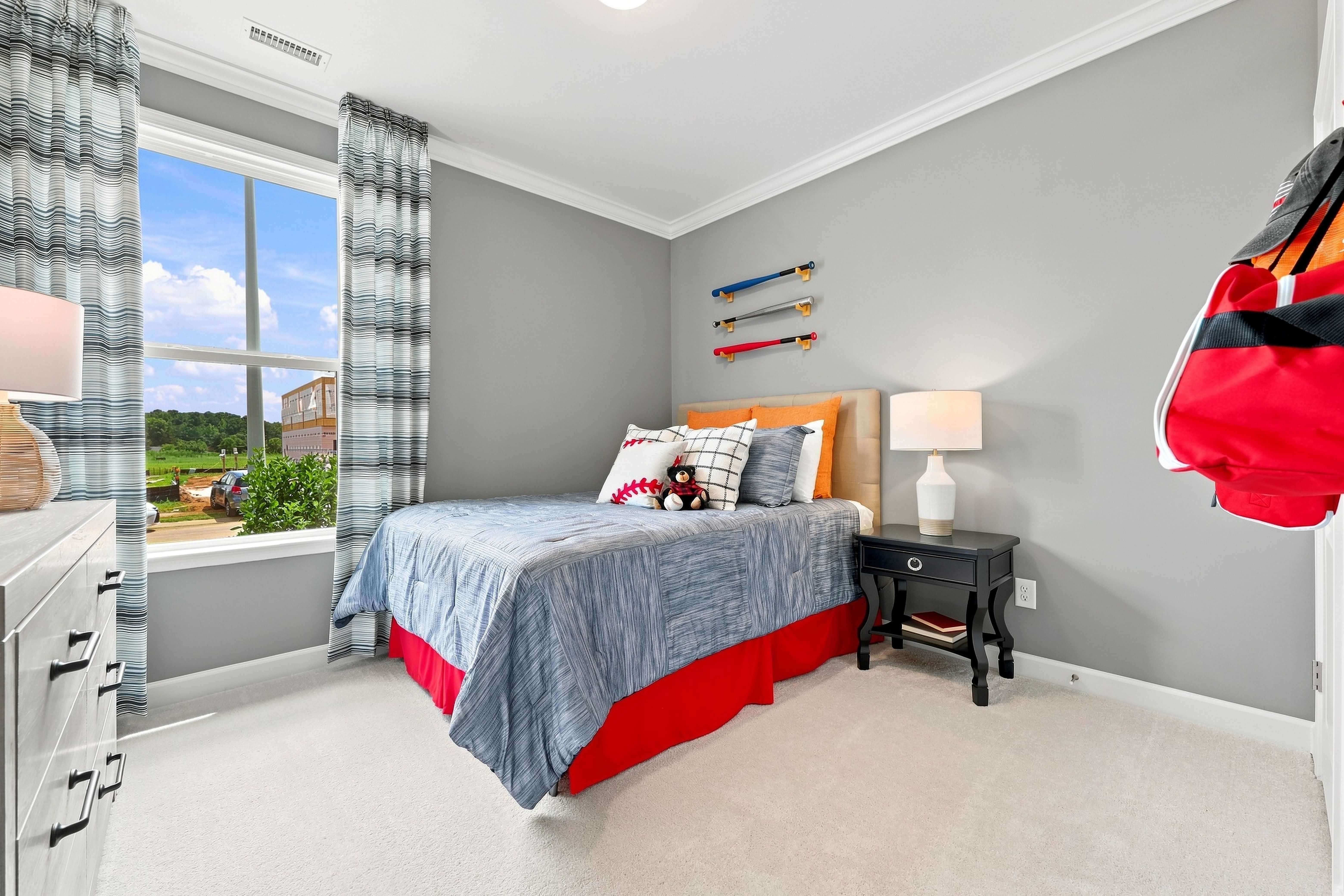 Cozy secondary bedroom in The Daphne D model home featuring baseball-themed decor, plush bedding, and natural lighting.