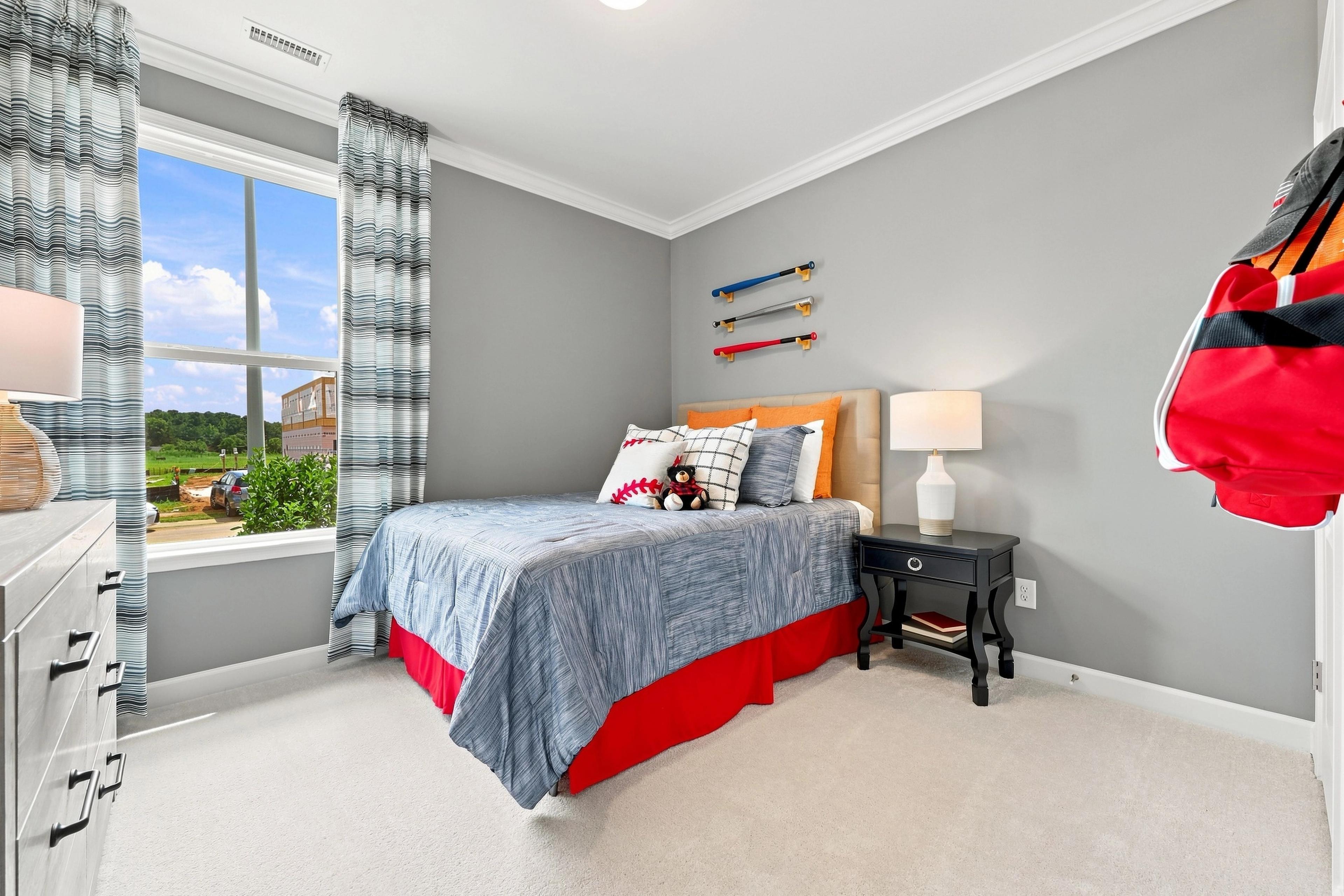 Cozy secondary bedroom in The Daphne D model home featuring baseball-themed decor, plush bedding, and natural lighting.