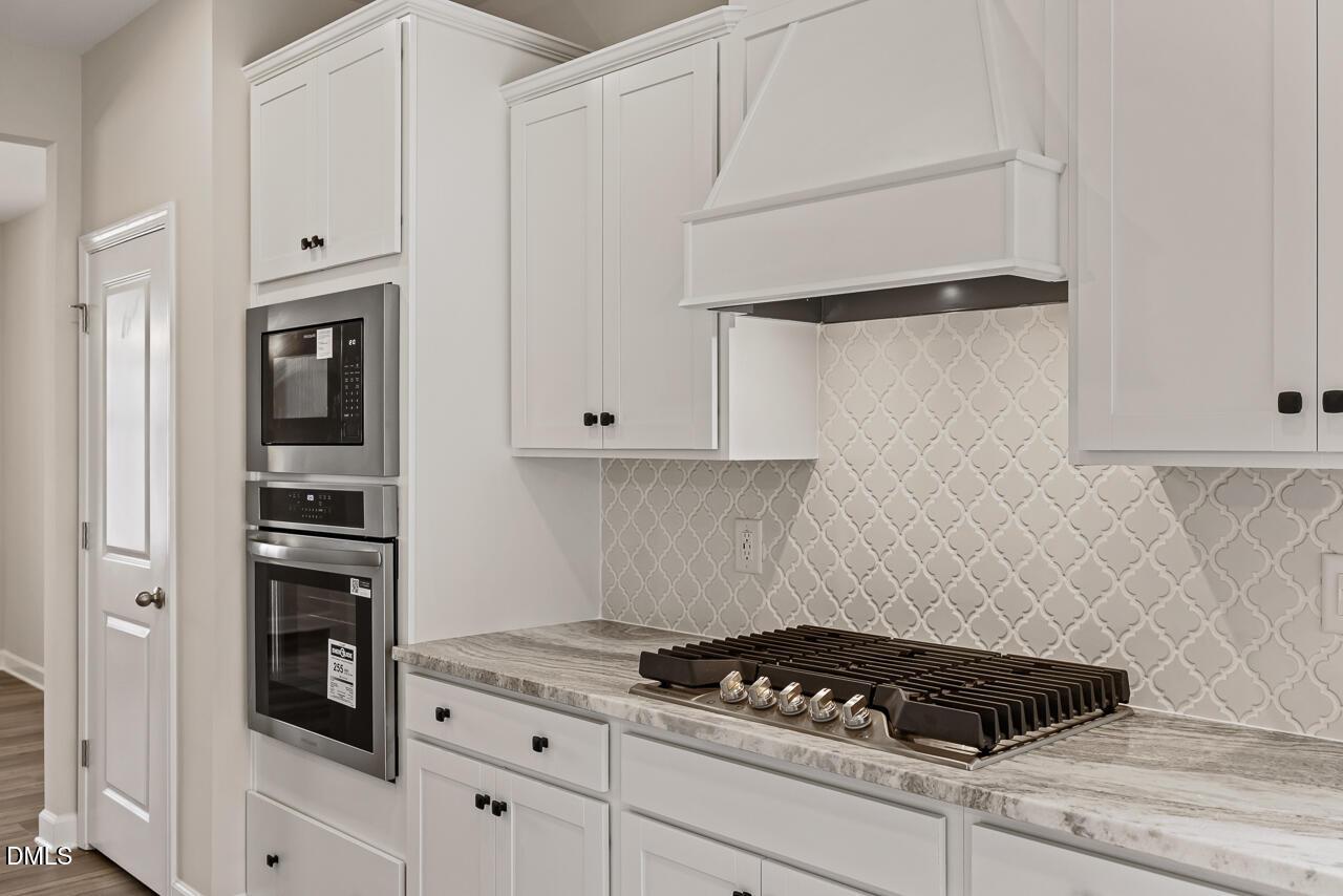 Modern white kitchen with built-in oven, gas cooktop, and stylish backsplash in The Ash C floor plan, Zebulon, NC.