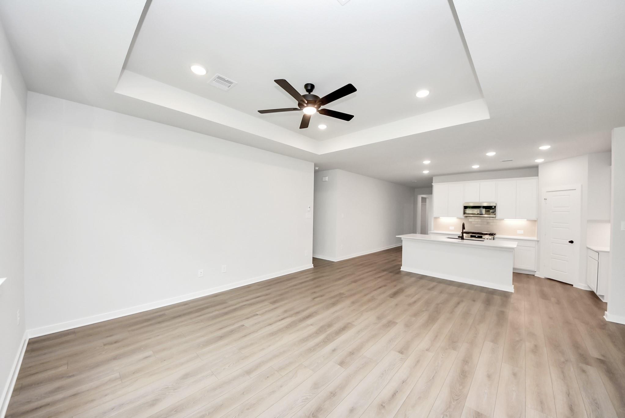 Open-concept living room with tray ceiling and modern kitchen in The Daphne F home at Sundance Cove, Crosby, Texas.