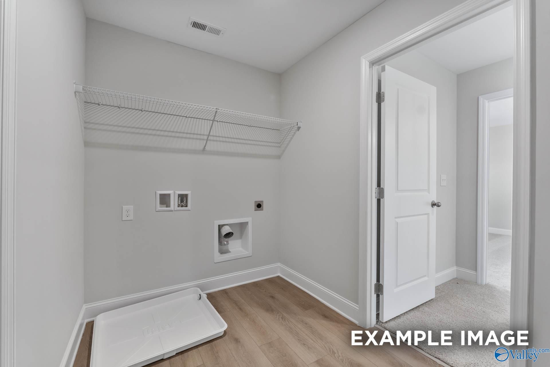 Spacious laundry room with gray walls, wire shelving, washer dryer hookups, and hardwood floors in Davidson Homes The Chelsea D, New Market, Alabama