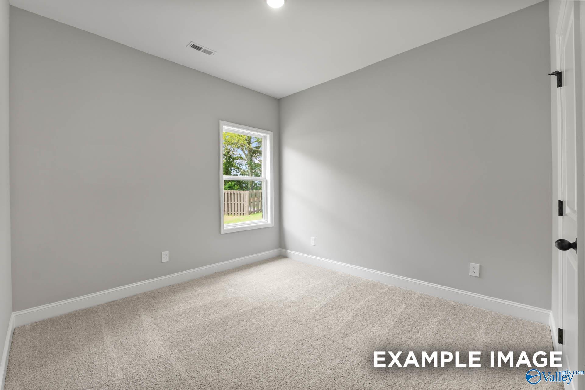 Spacious empty bedroom with gray walls, beige carpet, and window overlooking fenced backyard in Davidson Homes The Asheville C, Hazel Green, AL
