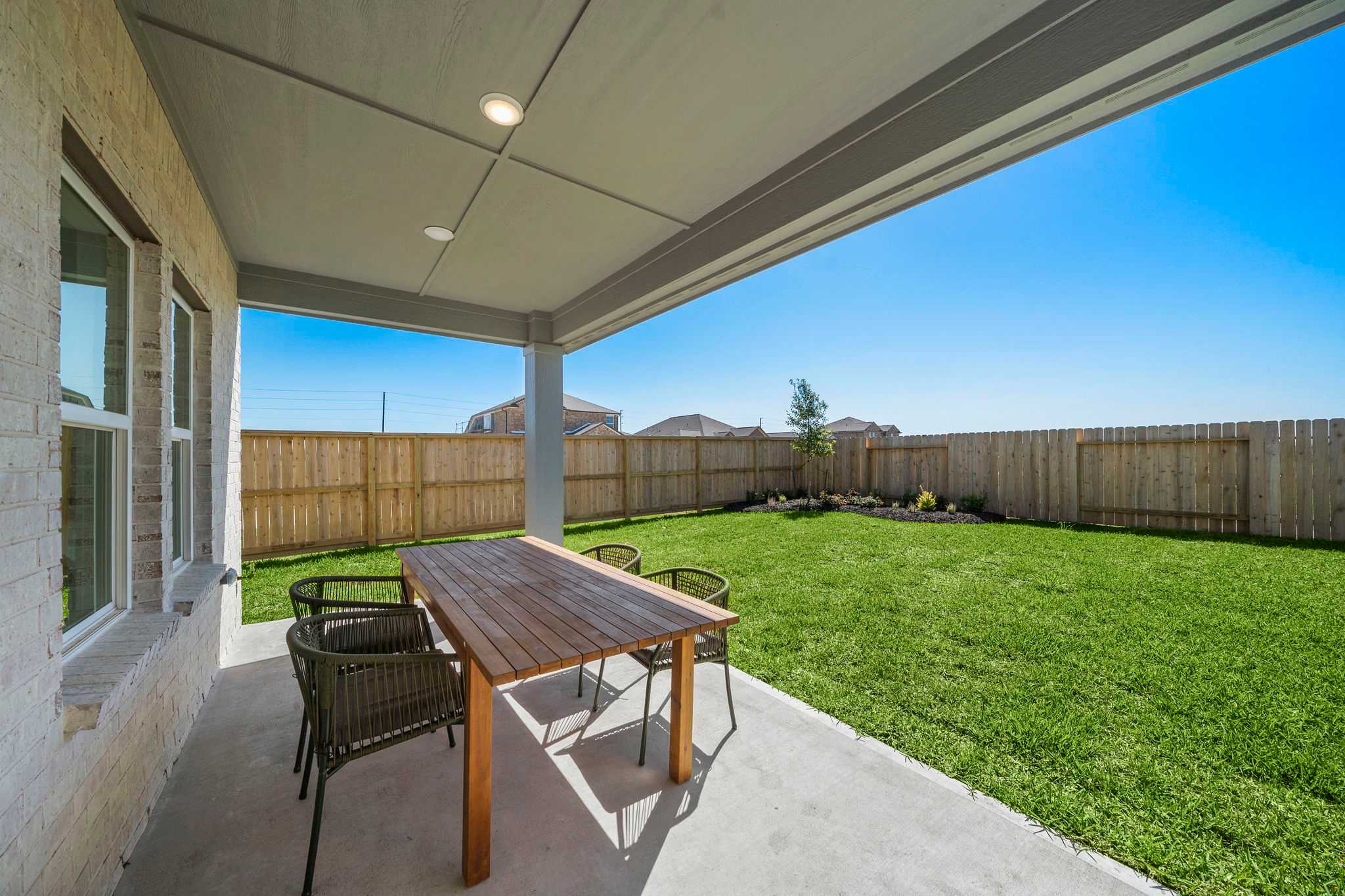 Spacious covered patio with wooden dining table and chairs in lush green backyard at River Ranch Meadows, Dayton TX