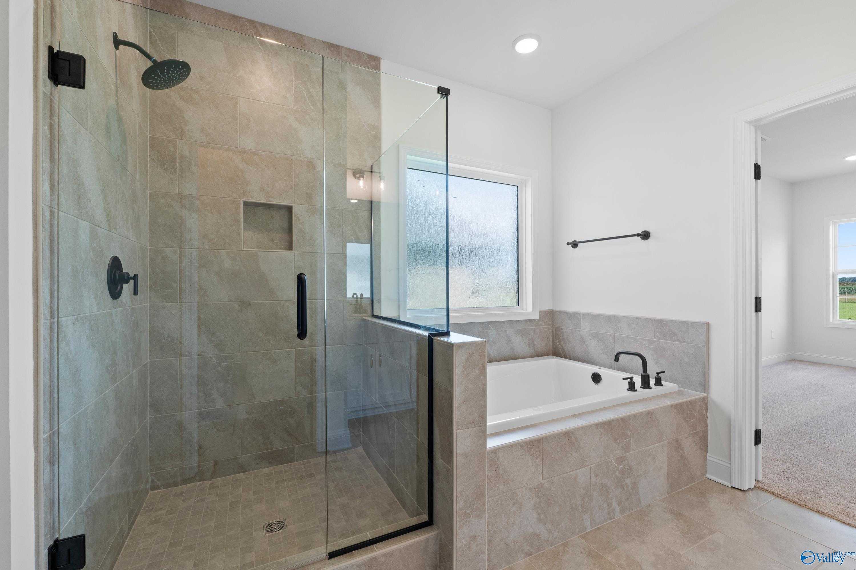 Modern master bathroom featuring frameless glass shower, soaking tub, and neutral tile in Davidson Homes The Rockford B, Toney, Alabama