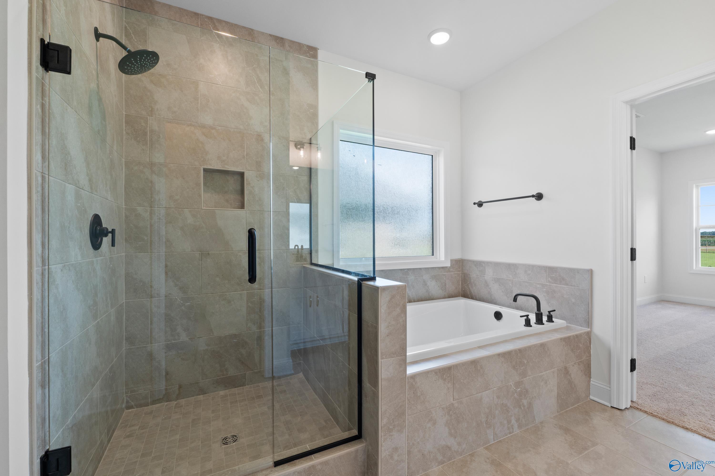 Elegant master bathroom featuring frameless glass shower, soaking tub, and beige tile in Davidson Homes The Rockford B, Toney, Alabama