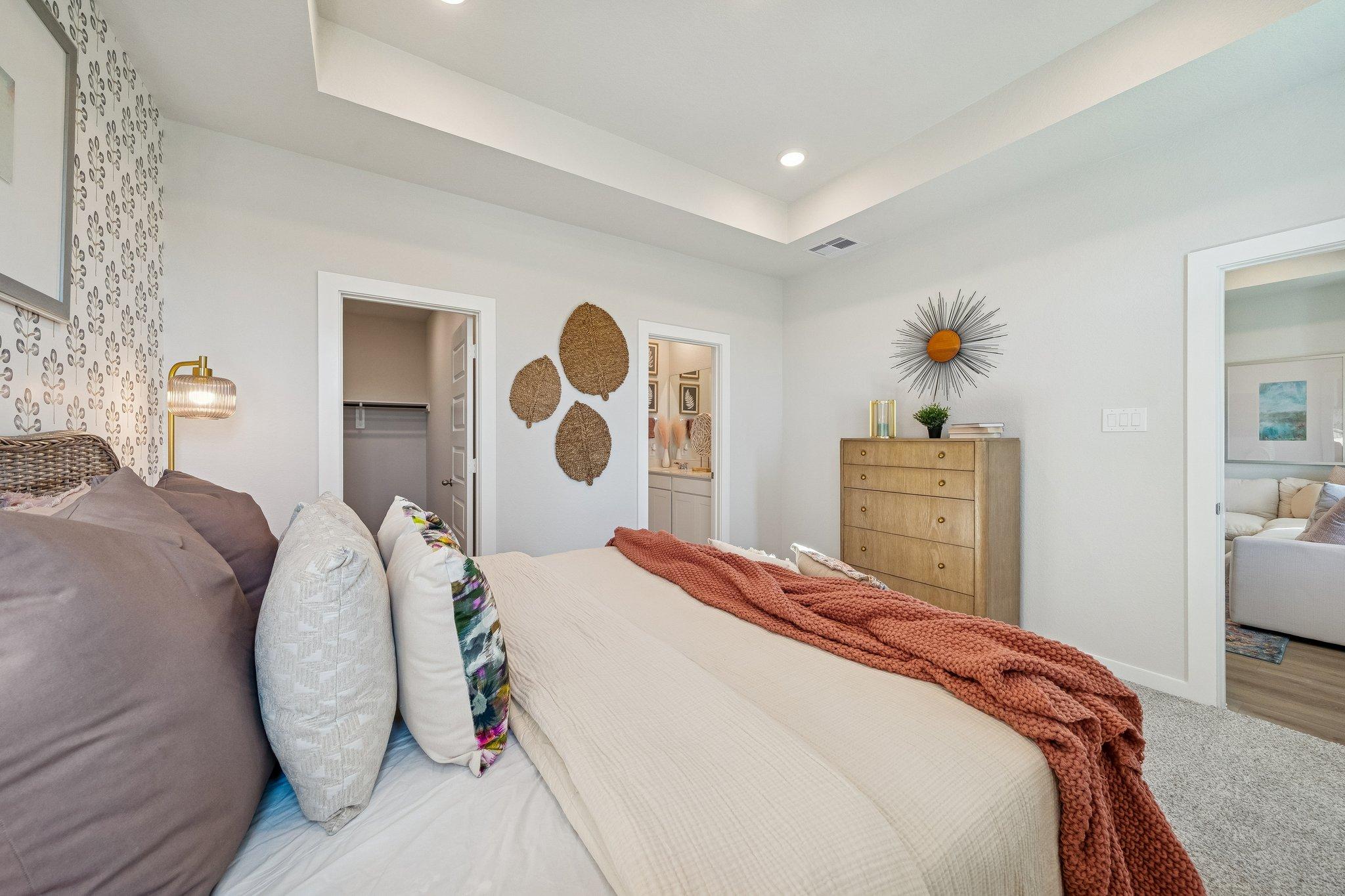 Spacious master bedroom at Spring Branch Crossing in Conroe Texas with king bed, woven wall art, sunburst decor and neutral palette