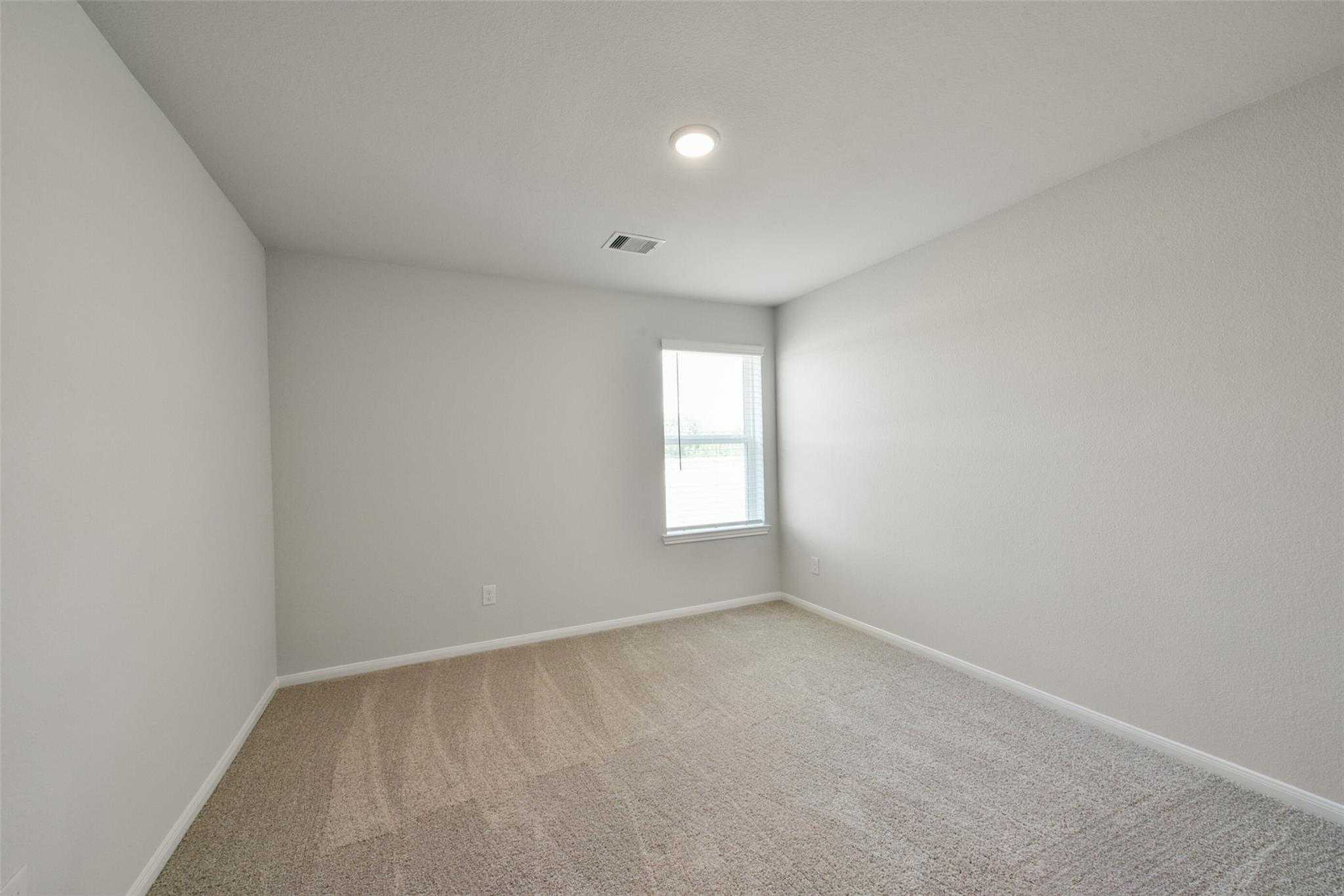 Empty bedroom with light gray walls, beige carpet flooring, and window with blinds in The Sabine E 4-bedroom home, Dayton, Texas