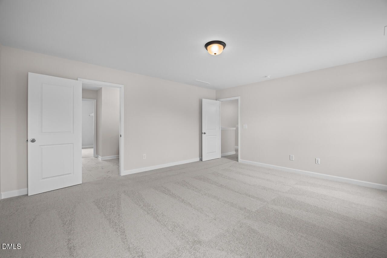 Spacious carpeted bedroom with neutral walls and double doors in The Willow B floor plan by Davidson Homes in Zebulon, NC.