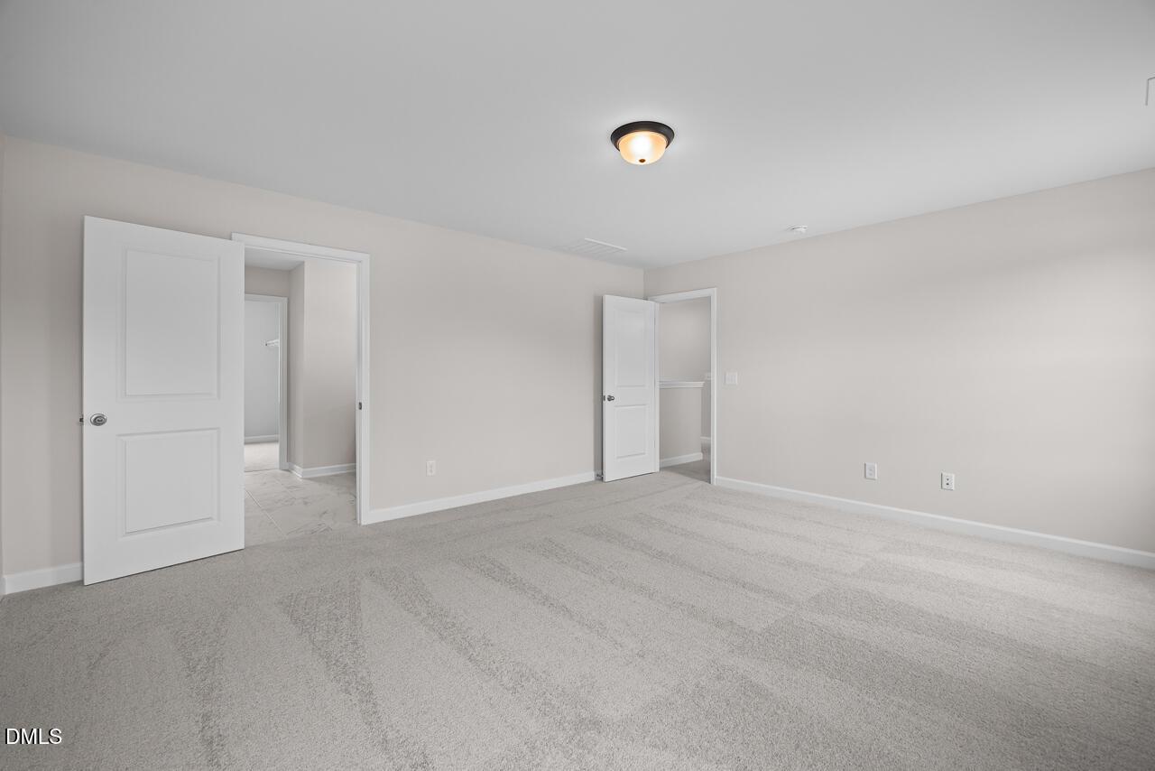Spacious carpeted bedroom with neutral walls and double doors in The Willow B floor plan by Davidson Homes in Zebulon, NC.