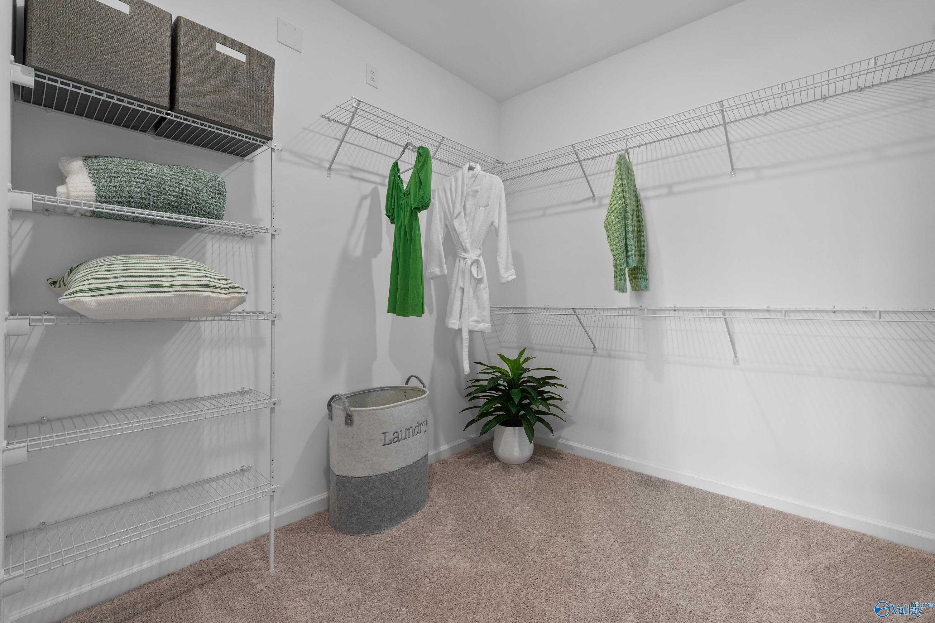 Spacious walk-in closet with wire shelving, hanging green dress and robe, storage bins, laundry basket in Evermore Homes The Malibu, Madison, Alabama