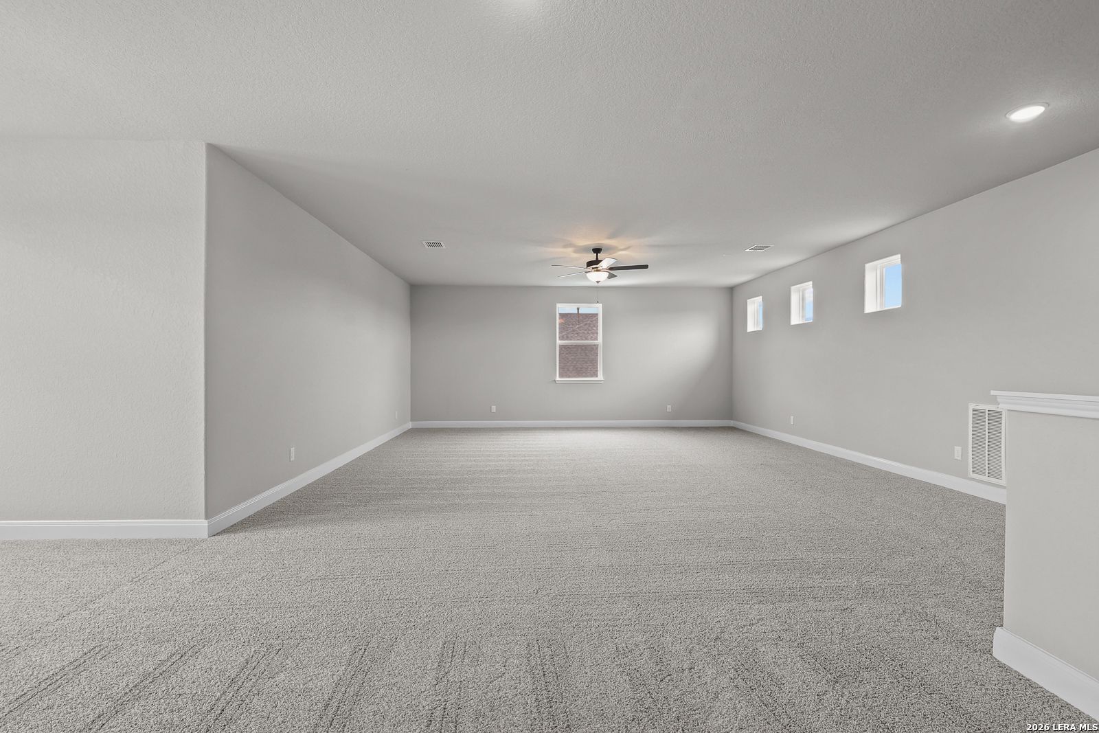 Spacious empty upstairs bonus room with gray carpet, light walls, ceiling fan, recessed lights, and windows in The Belmont H home, Castroville, Texas