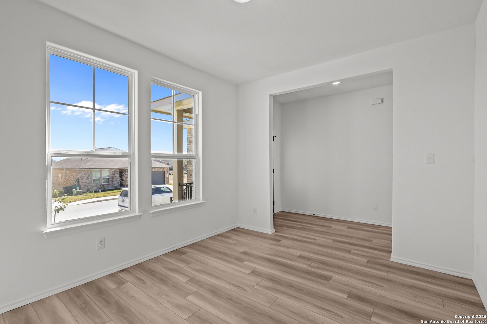 Bright empty room with large windows, wood floors, and front yard view in Davidson Homes The Douglas E, San Antonio, Texas