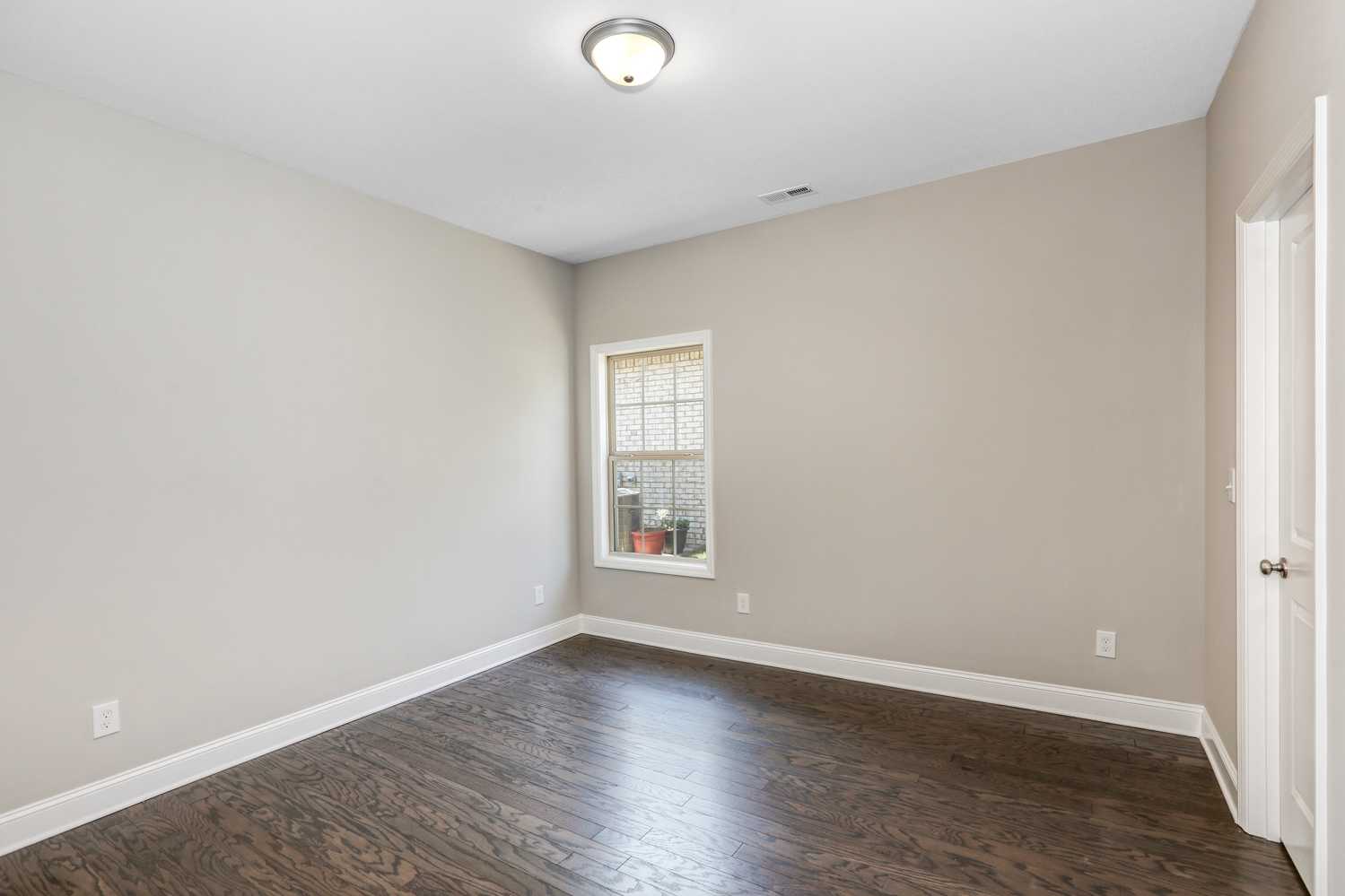Spacious bedroom in The Montgomery by Davidson Homes featuring beige walls, hardwood floors, and large window