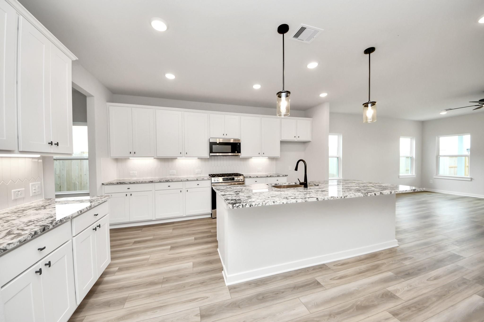 Modern kitchen with white cabinets, granite island, and wood-look floors in The Sorrento E at Sundance Cove, Crosby, Texas.