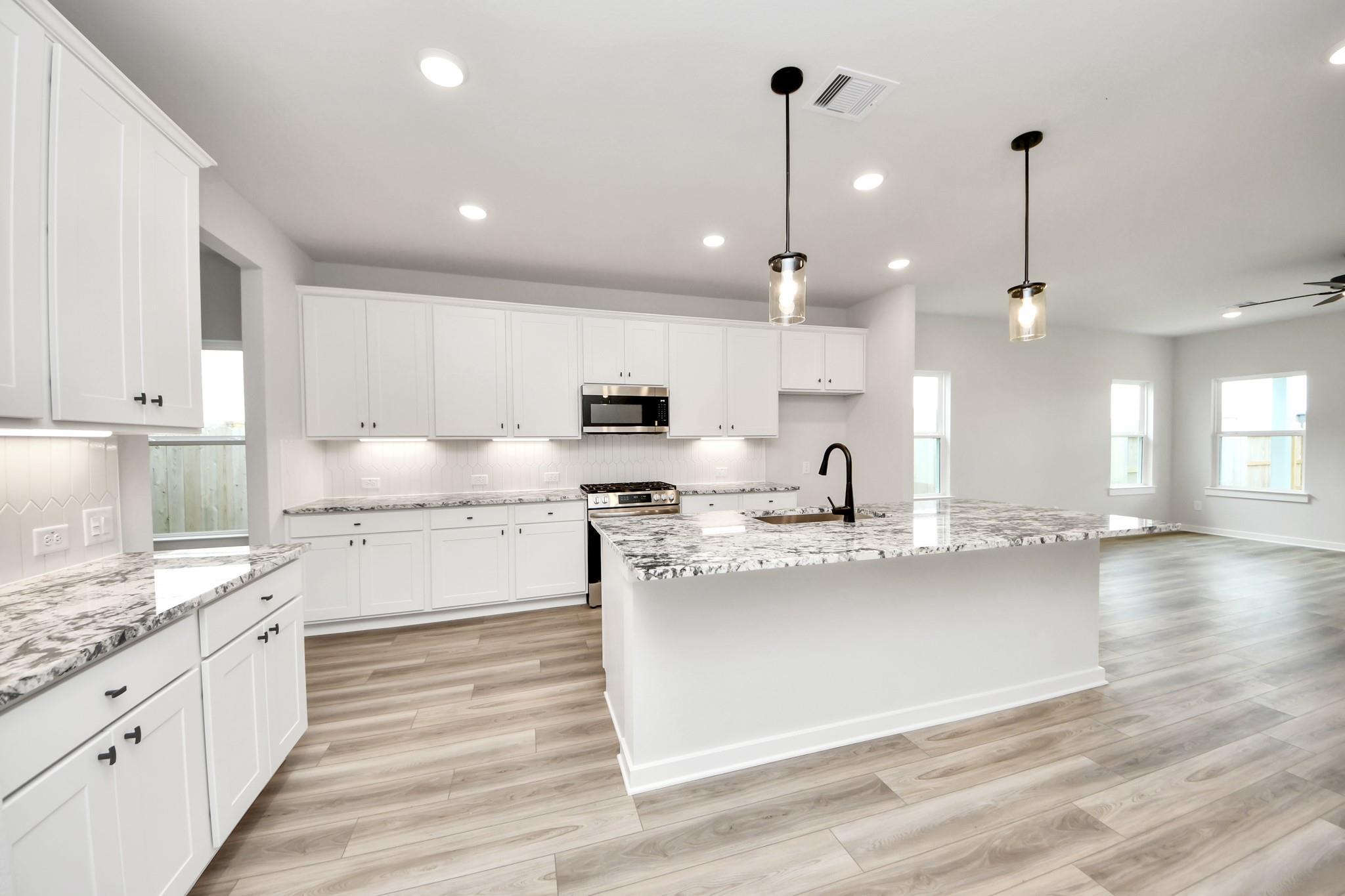 Modern kitchen with white cabinets, granite island, and wood-look floors in The Sorrento E at Sundance Cove, Crosby, Texas.