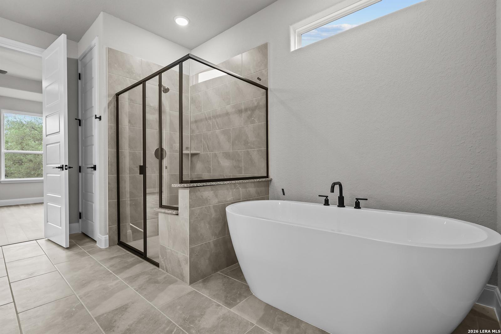 Elegant master bathroom with frameless glass shower, freestanding white tub, and beige tiles in Davidson Homes The Belmont H, Castroville, Texas