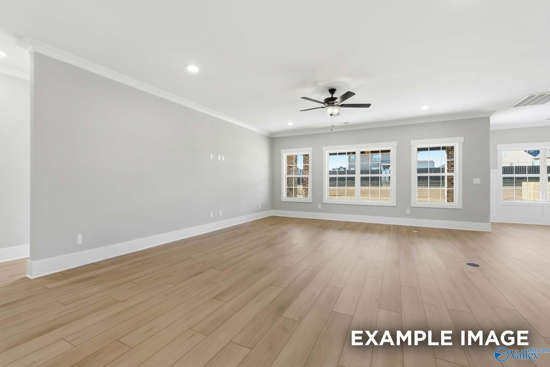 Bright living room with large triple windows, ceiling fan, recessed lights, and light oak hardwood floors in The Emory home, Decatur AL