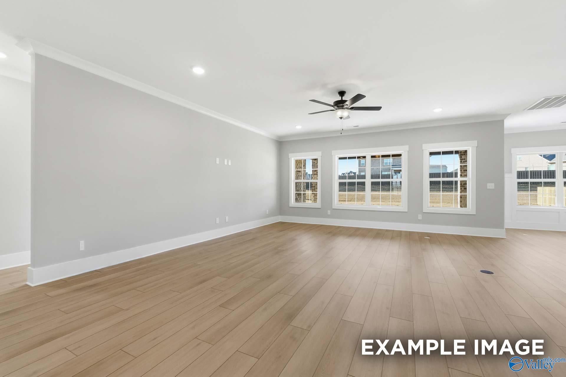 Bright living room with large triple windows, ceiling fan, recessed lights, and light oak hardwood floors in The Emory home, Decatur AL
