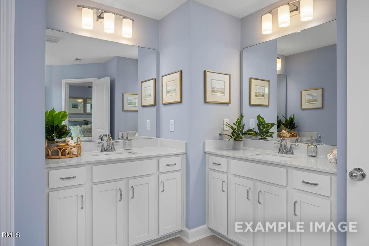 Spacious double vanity master bathroom with white cabinets, light blue walls, mirrors, and plants in Davidson Homes The Graham, Fuquay-Varina, NC