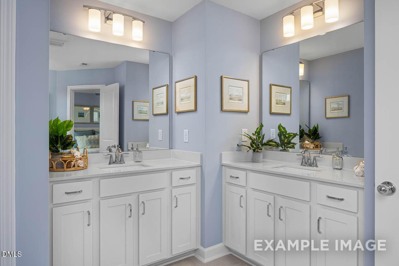 Elegant double vanity bathroom with light blue walls, white cabinets, mirrors and plants in Davidson Homes The Graham Interior, Fuquay-Varina, NC