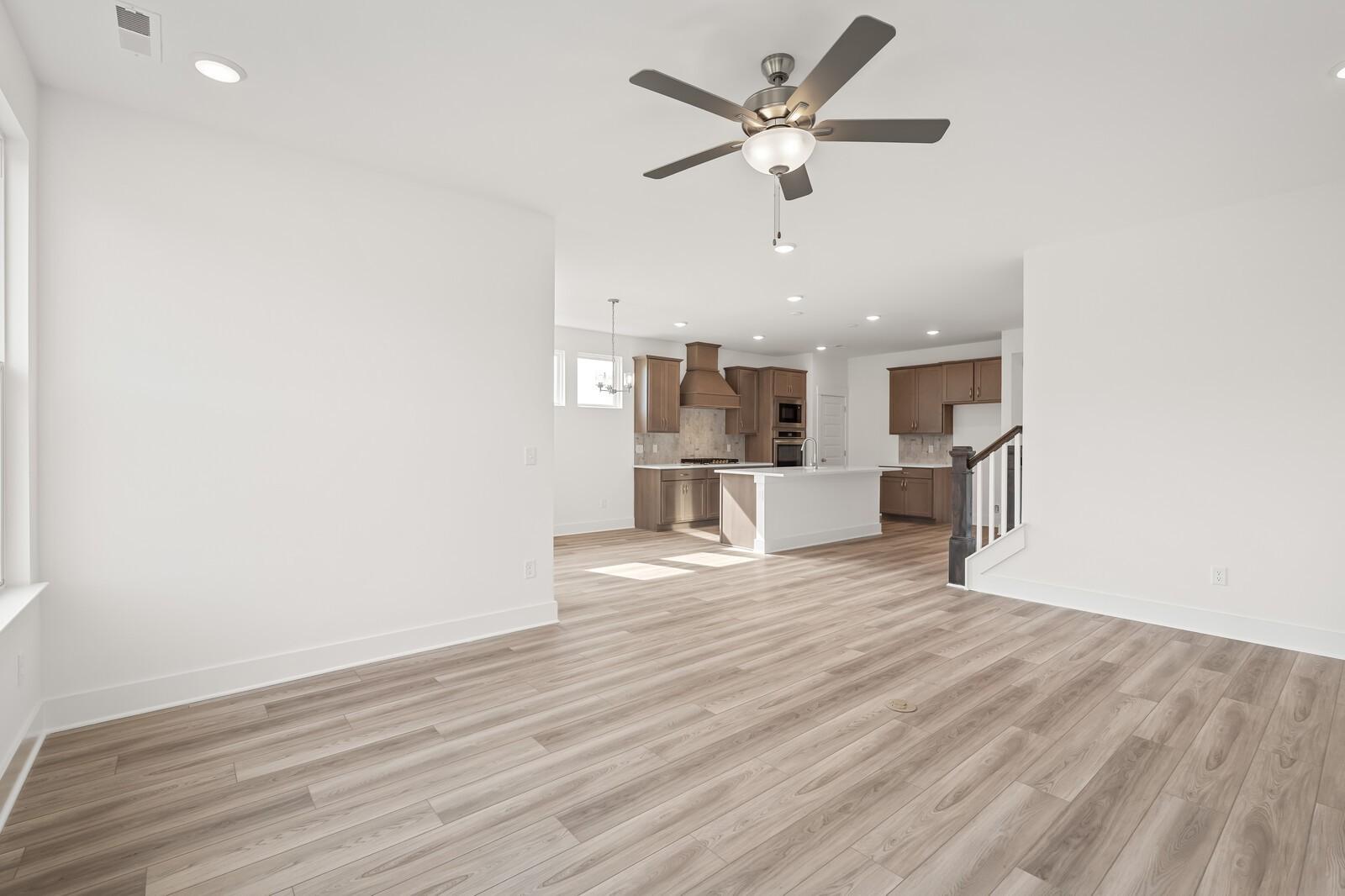 Open-concept living and kitchen with hardwood floors, white cabinets, island, and ceiling fan in Davidson Homes The Ash C, Mt. Juliet, TN