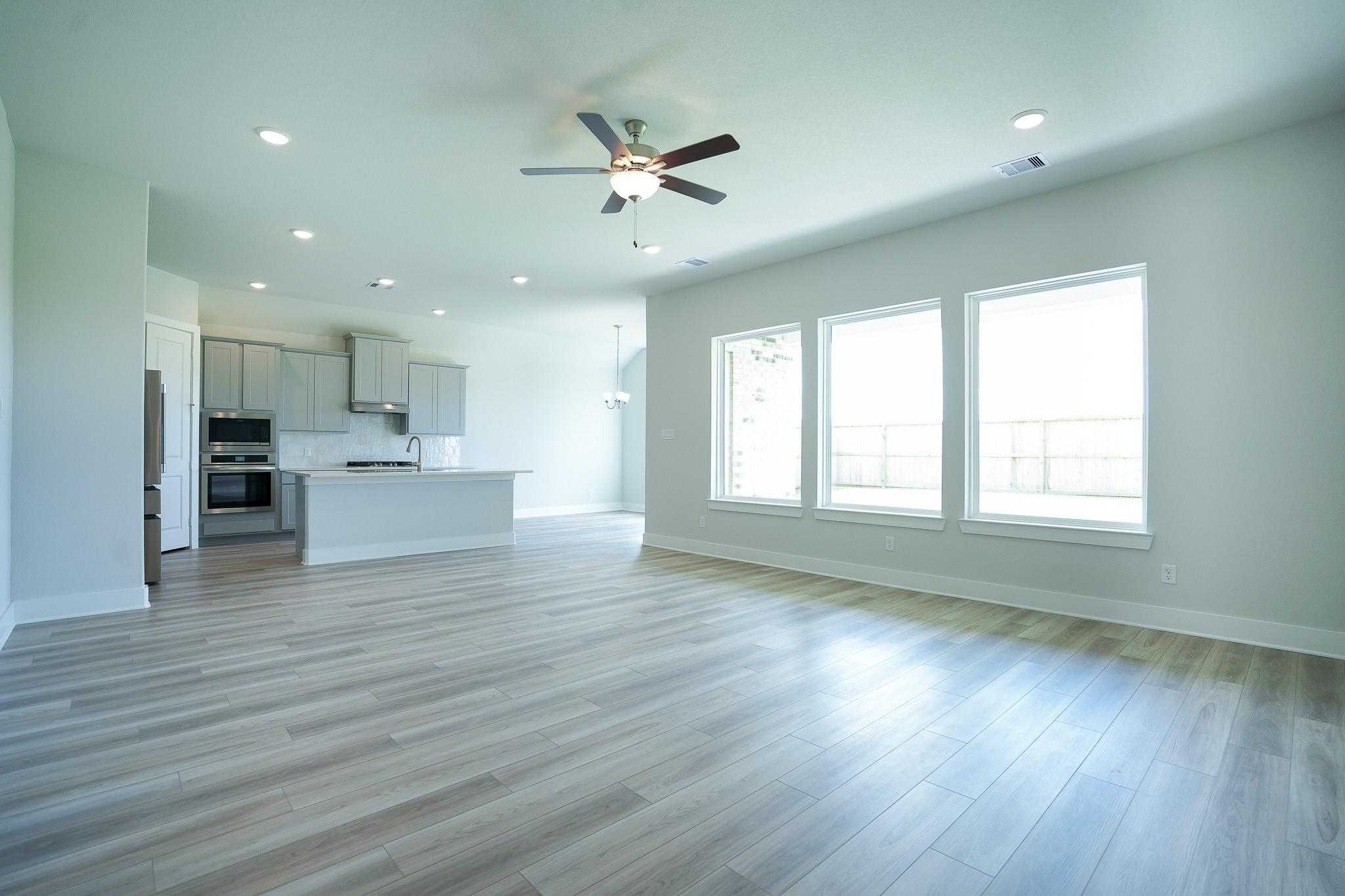 Bright open-concept living room and kitchen with laminate flooring, white cabinets, and large windows in Davidson Homes The Edward A, Lago Mar