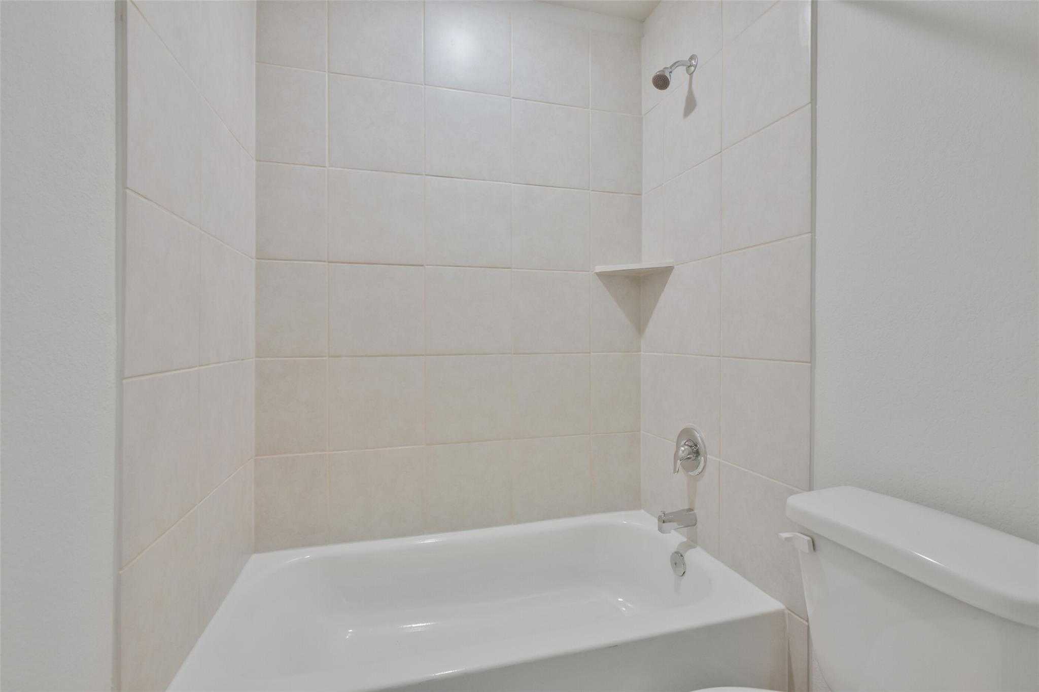 Modern white-tiled bathroom with soaking tub, walk-in shower, and toilet in Davidson Homes The Tierra A, Dayton, Texas