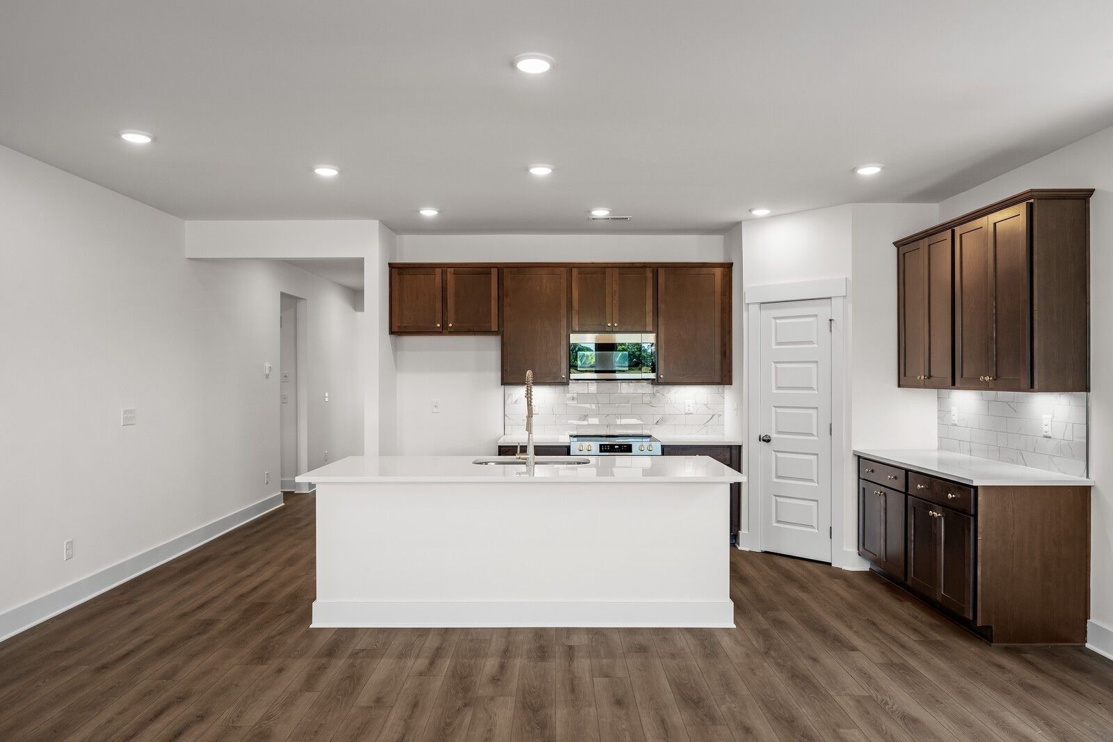 Modern kitchen with white island, dark wood cabinets, and hardwood floors in Davidson Homes Cottonwood E plan, Gallatin, TN