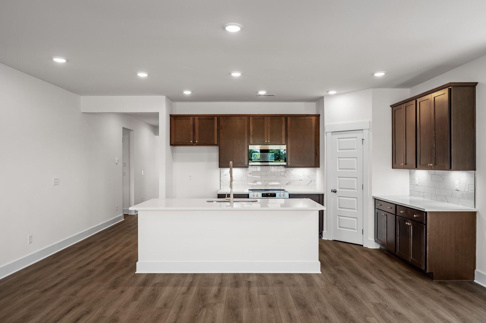 Modern kitchen with white island, dark wood cabinets, and hardwood floors in Davidson Homes Cottonwood E plan, Gallatin, TN