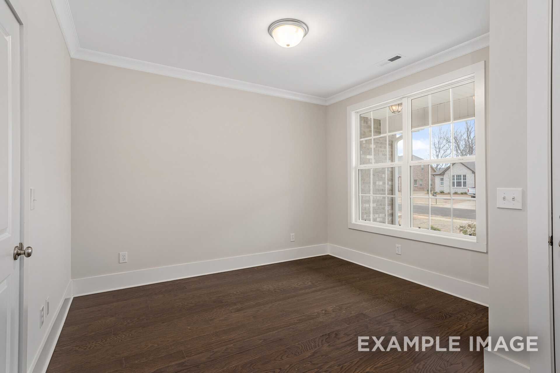 Spacious secondary bedroom in The Rockford floor plan with beige walls, hardwood floors, and large window overlooking neighborhood