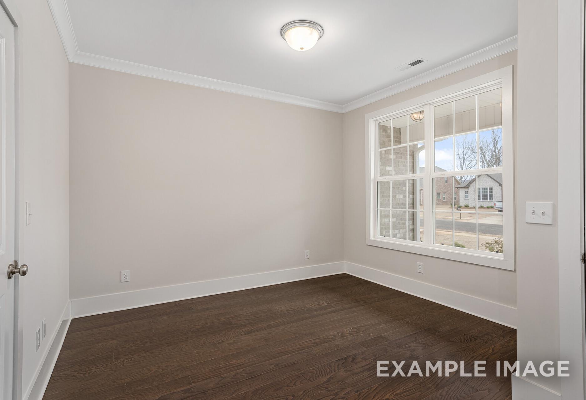 Spacious secondary bedroom in The Rockford floor plan with beige walls, hardwood floors, and large window overlooking neighborhood