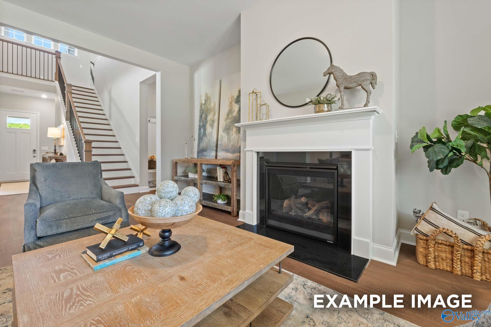 Cozy living room featuring white gas fireplace, gray velvet armchair, wooden coffee table, and open staircase in Evermore Homes The Haven E, Owens Cross Roads, Alabama