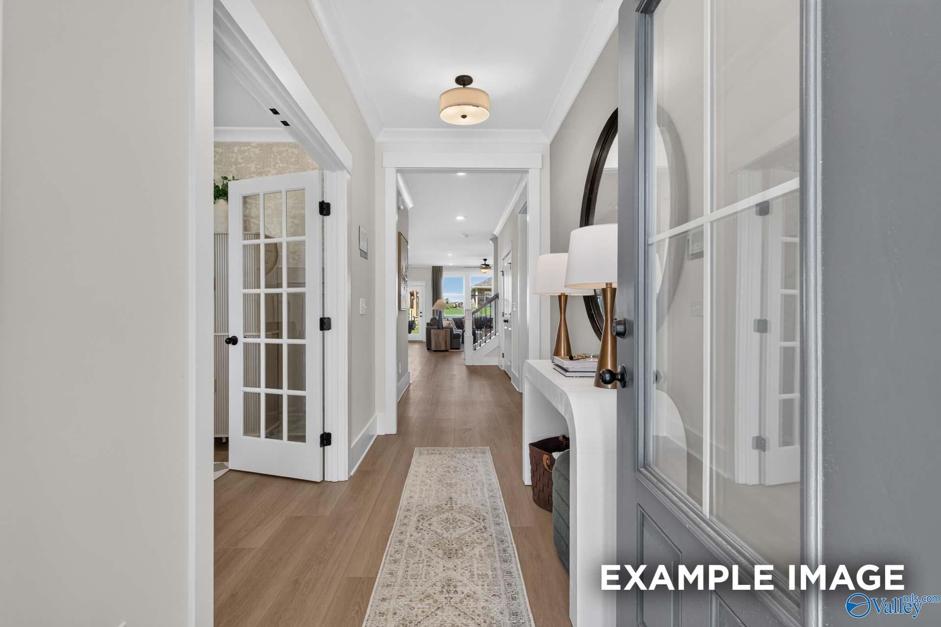 Bright foyer with glass-panel door, console table, round mirror, and hardwood floors in Davidson Homes Ashport K, Hazel Green, Alabama