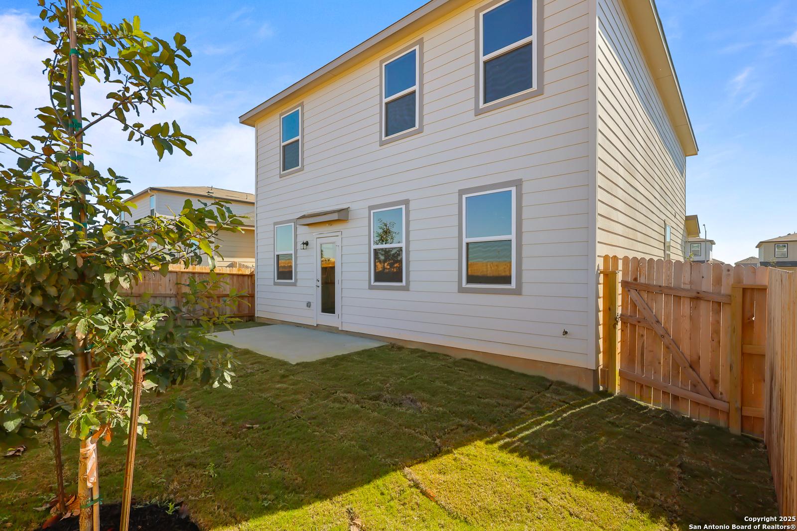 Two-story beige home exterior with fenced backyard, concrete patio, young tree, and lush grass in Applewhite Meadows, San Antonio